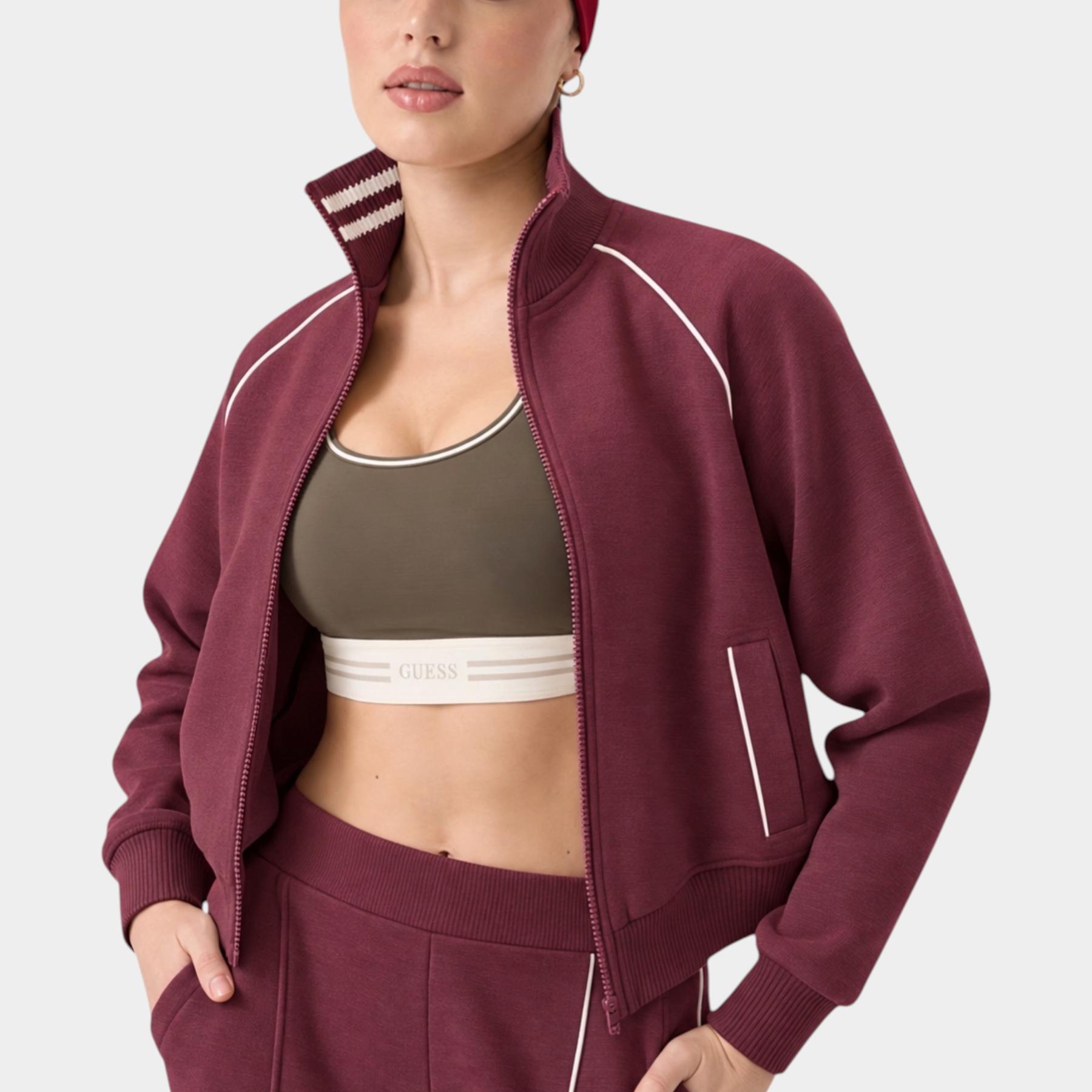 Modella indossa felpa full zip bordeaux GUESS con dettagli a righe sul colletto e fascia per capelli coordinata