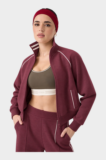 Modella indossa felpa full zip bordeaux GUESS con dettagli a righe sul colletto e fascia per capelli coordinata