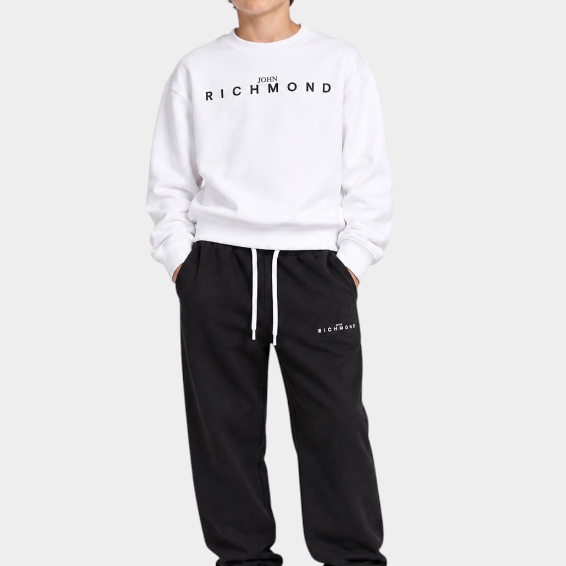 Ragazzo indossa completo sportivo Follower SRL con felpa bianca e pantaloni neri con logo Richmond