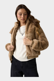 Modella indossa un bomber beige in pelliccia sintetica con cappuccio di Follower SRL, abbinato a maglia bianca