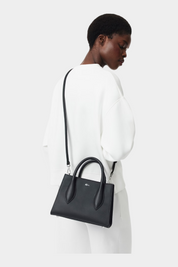 Modella indossa una borsa a mano nera LACOSTE Daily City con tracolla, venduta da Follower SRL