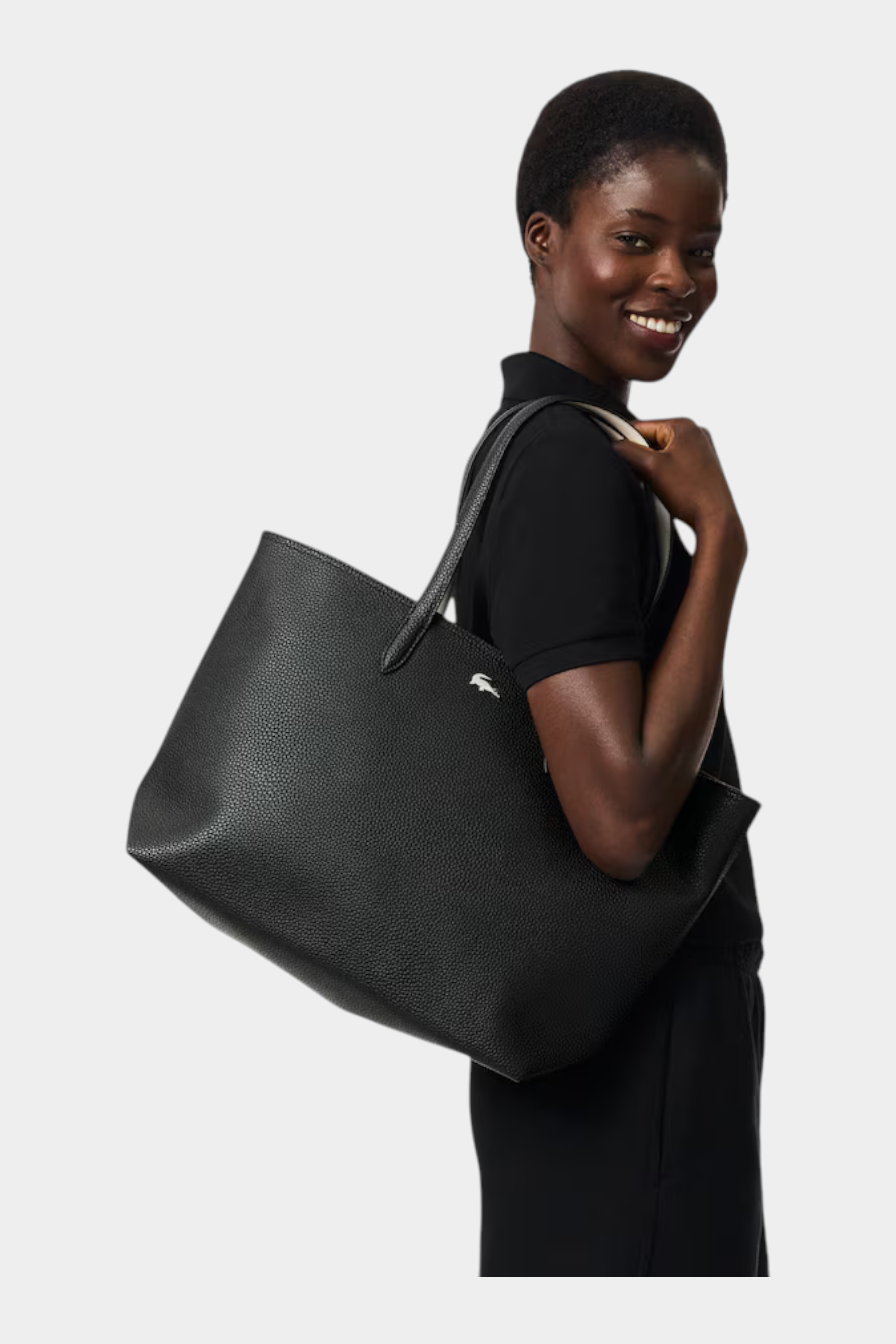 Modella sorridente indossa una borsa tote nera con zip LACOSTE di Follower SRL in pelle martellata
