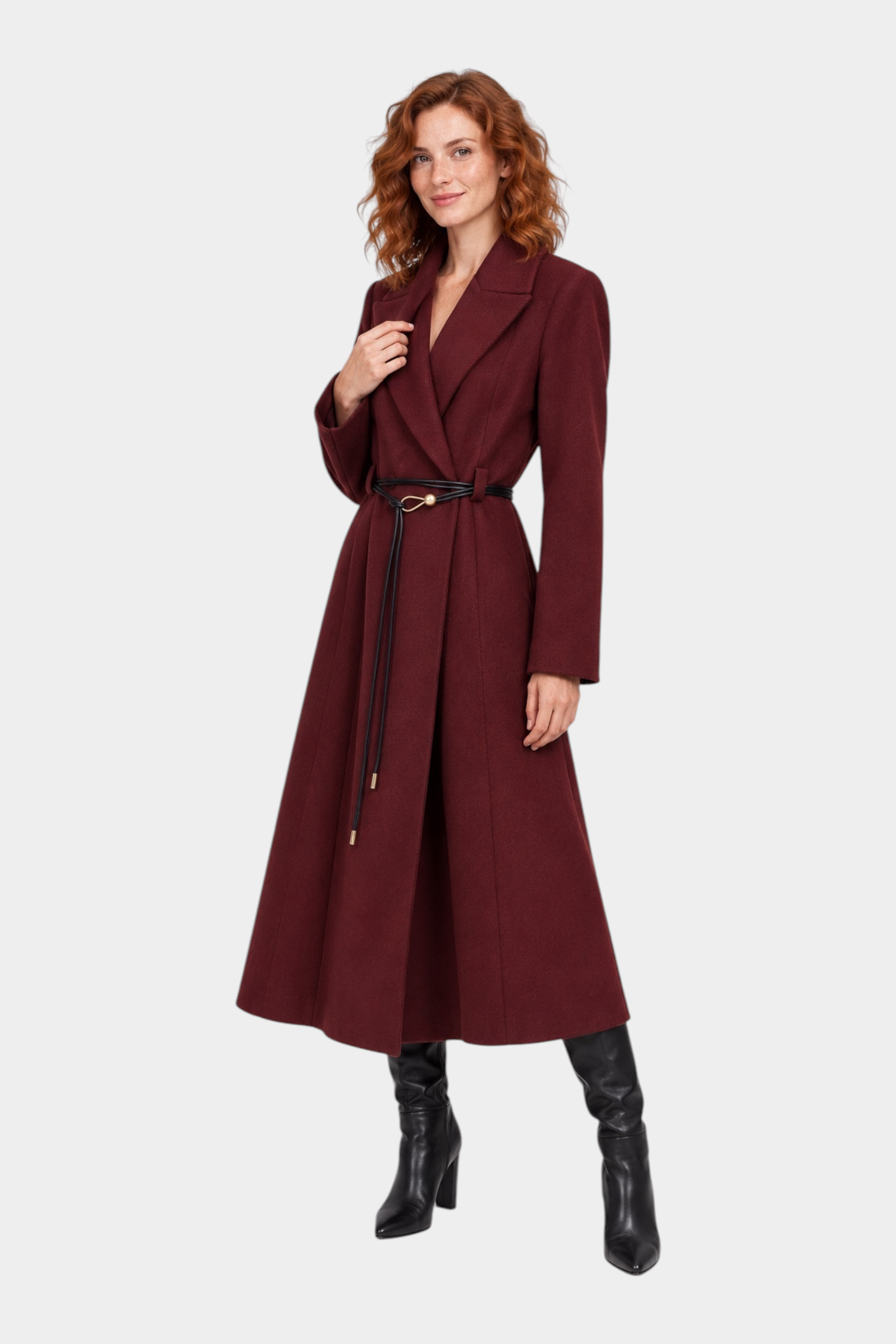 Modella indossa un cappotto lungo bordeaux Follower SRL con cintura sottile in vita e stivali neri