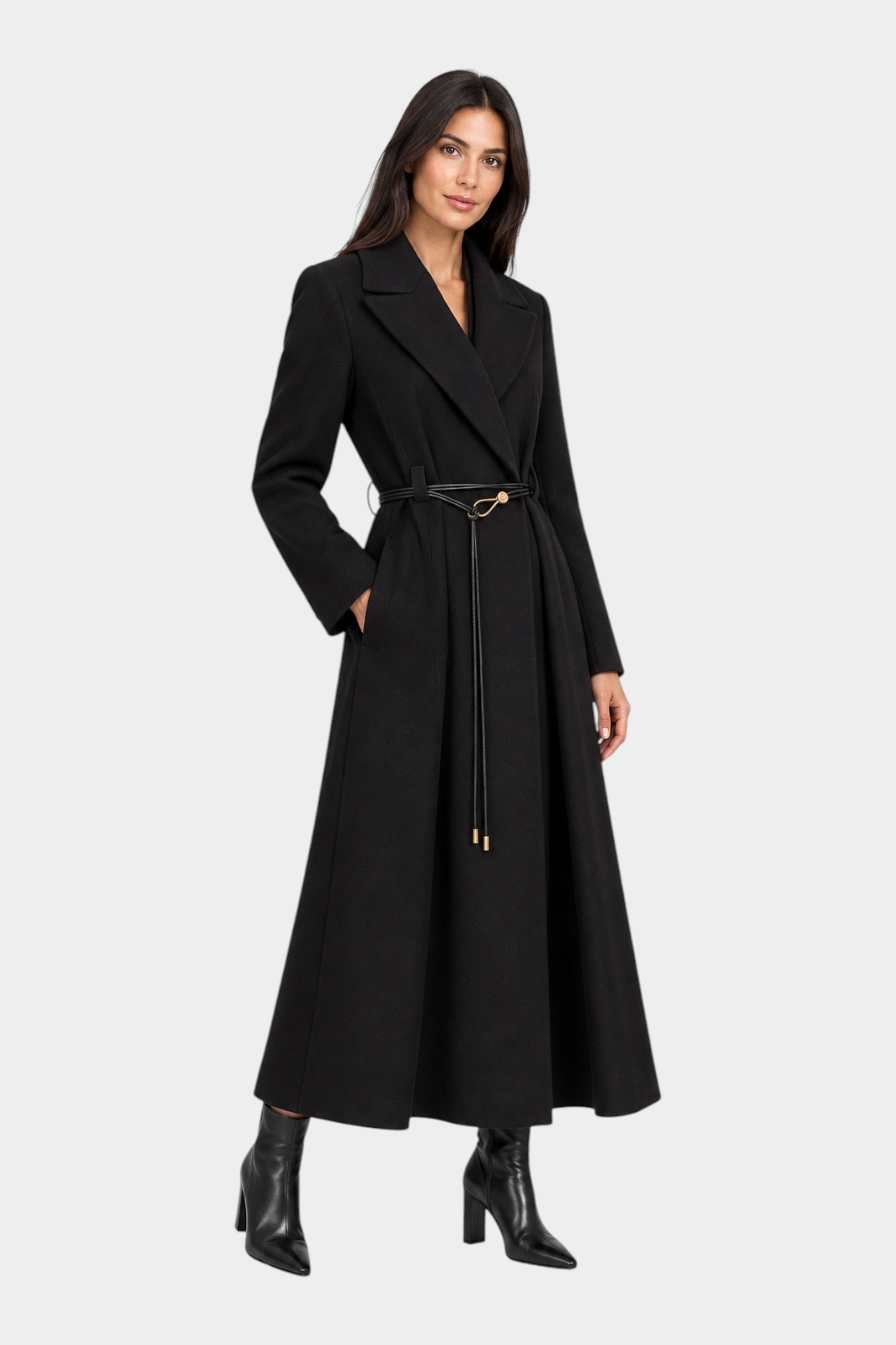 Modella indossa un cappotto lungo nero Follower SRL con cintura sottile in vita e revers ampi su fondo grigio