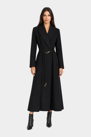 Modella indossa un cappotto lungo nero Follower SRL con cintura sottile in vita e stivaletti coordinati