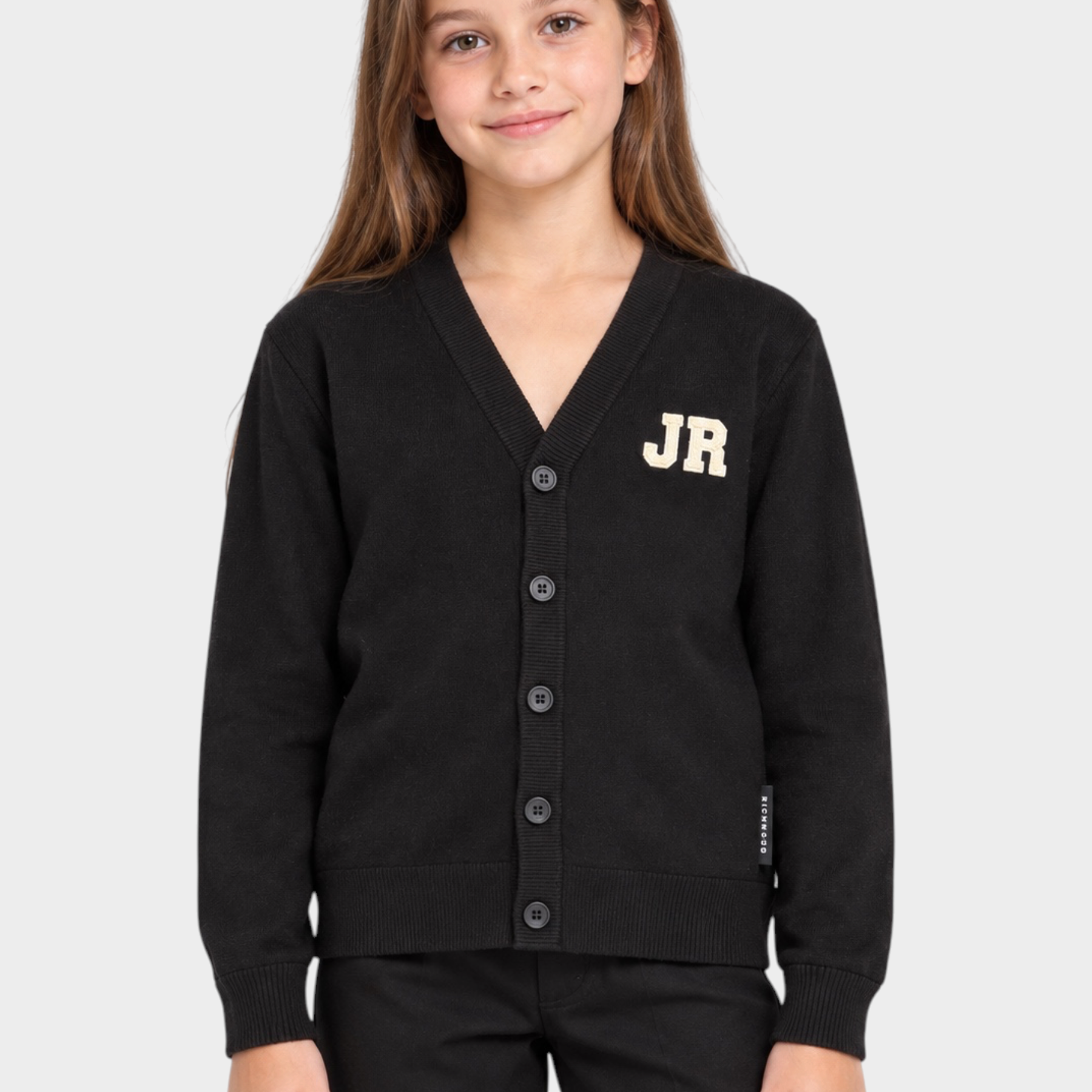Bambina che indossa un cardigan nero Follower SRL con scollo a V, bottoni e logo JR ricamato sul petto