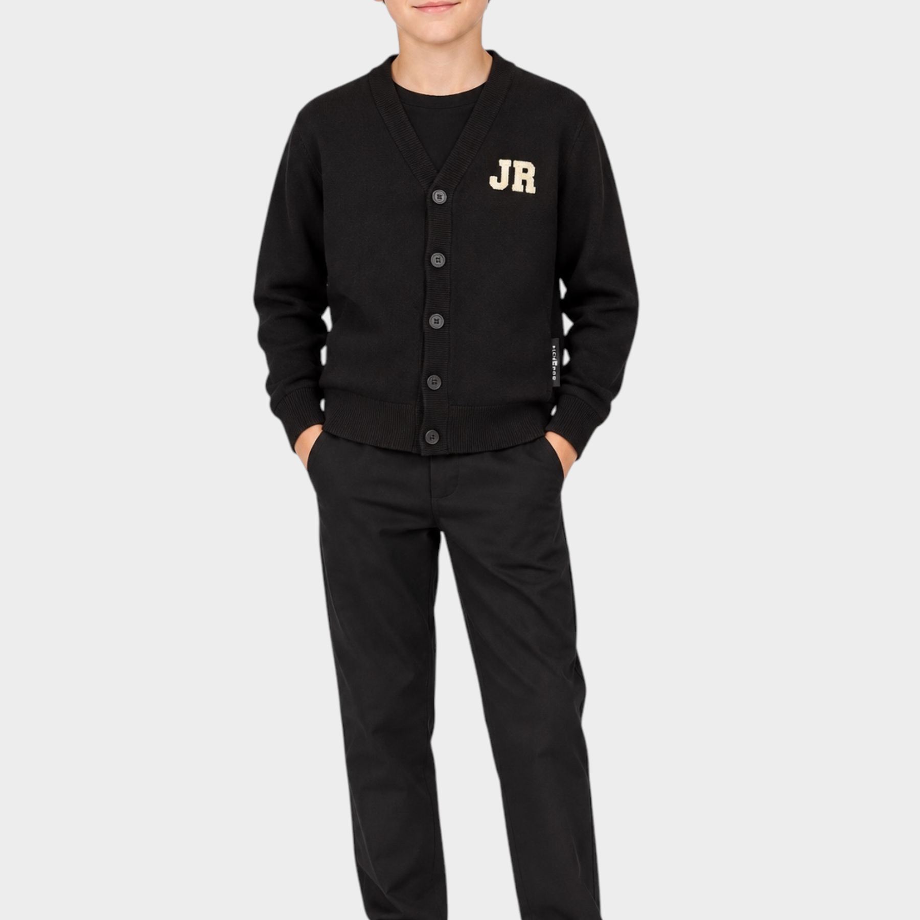 Ragazzo che indossa un cardigan nero Follower SRL con logo iconico JR, pantaloni neri e scarpe da ginnastica bianche