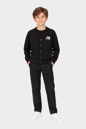 Ragazzo che indossa un cardigan nero Follower SRL con logo iconico JR, pantaloni neri e scarpe da ginnastica bianche