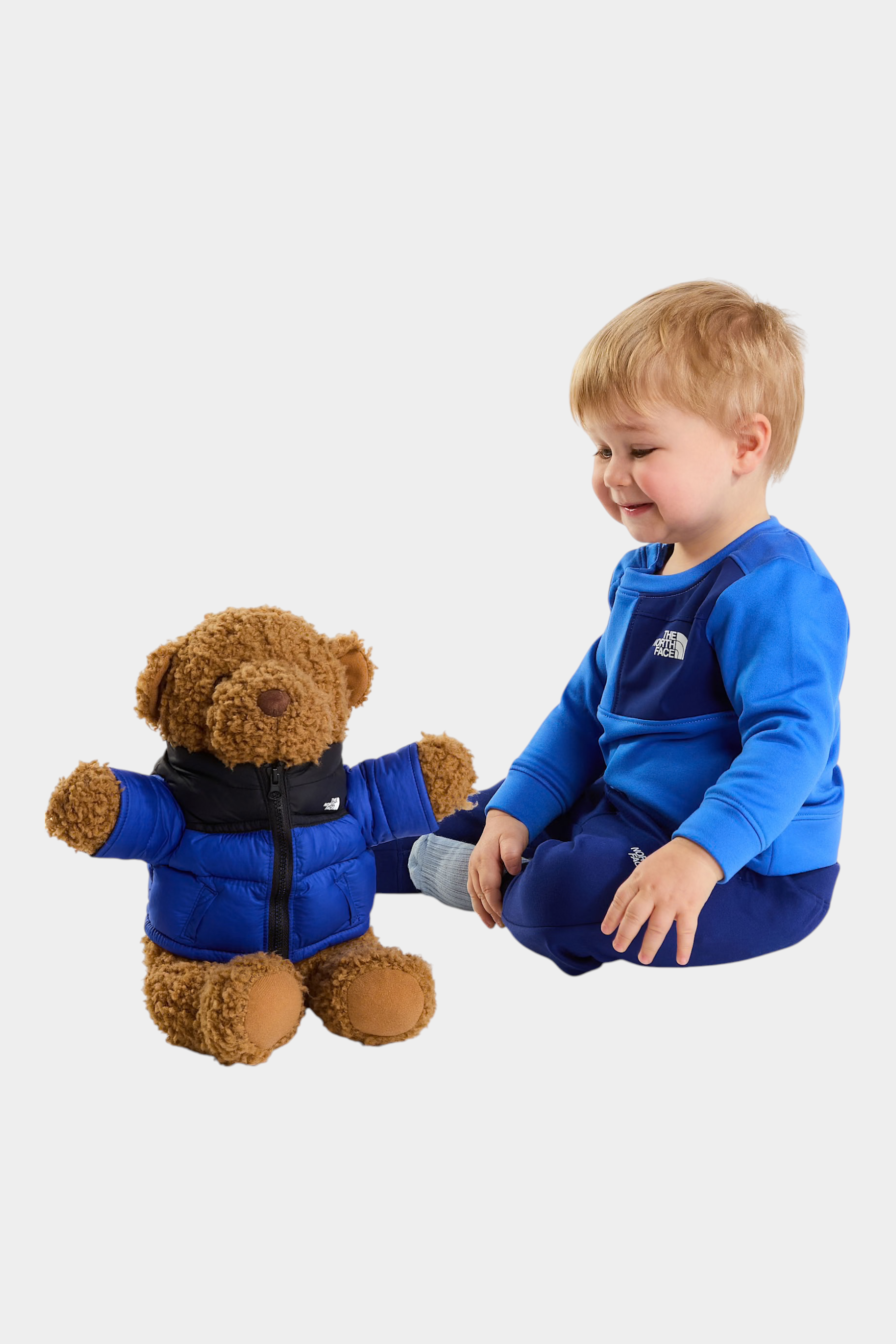 Bambino che gioca con un orsacchiotto indossando un completo due pezzi blu The North Face di Follower SRL