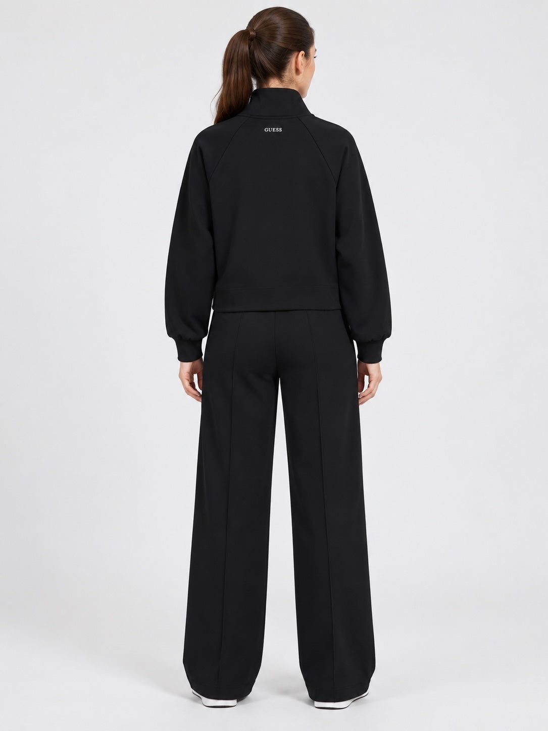 Donna che indossa un completo nero Follower SRL composto da felpa con logo GUESS e pantaloni jogger a gamba larga