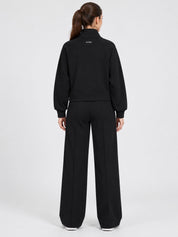 Donna che indossa un completo nero Follower SRL composto da felpa con logo GUESS e pantaloni jogger a gamba larga