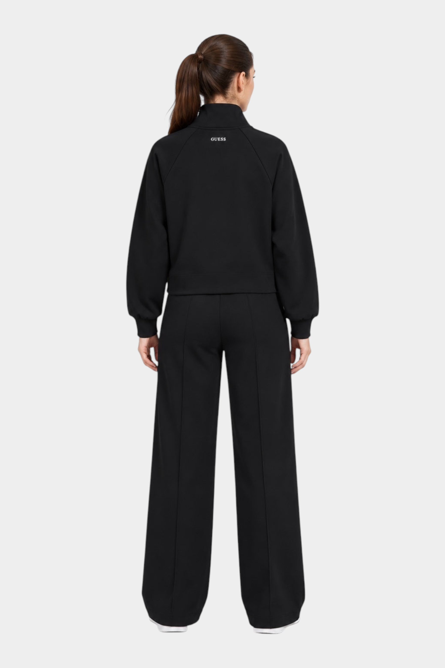 Donna che indossa un completo nero Follower SRL composto da felpa con logo GUESS e pantaloni jogger a gamba larga