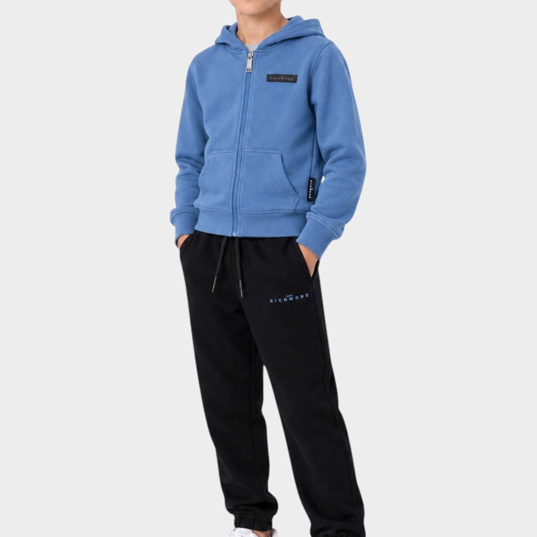 Ragazzo indossa completo sportivo Follower SRL con felpa azzurra con zip e pantaloni neri in cotone