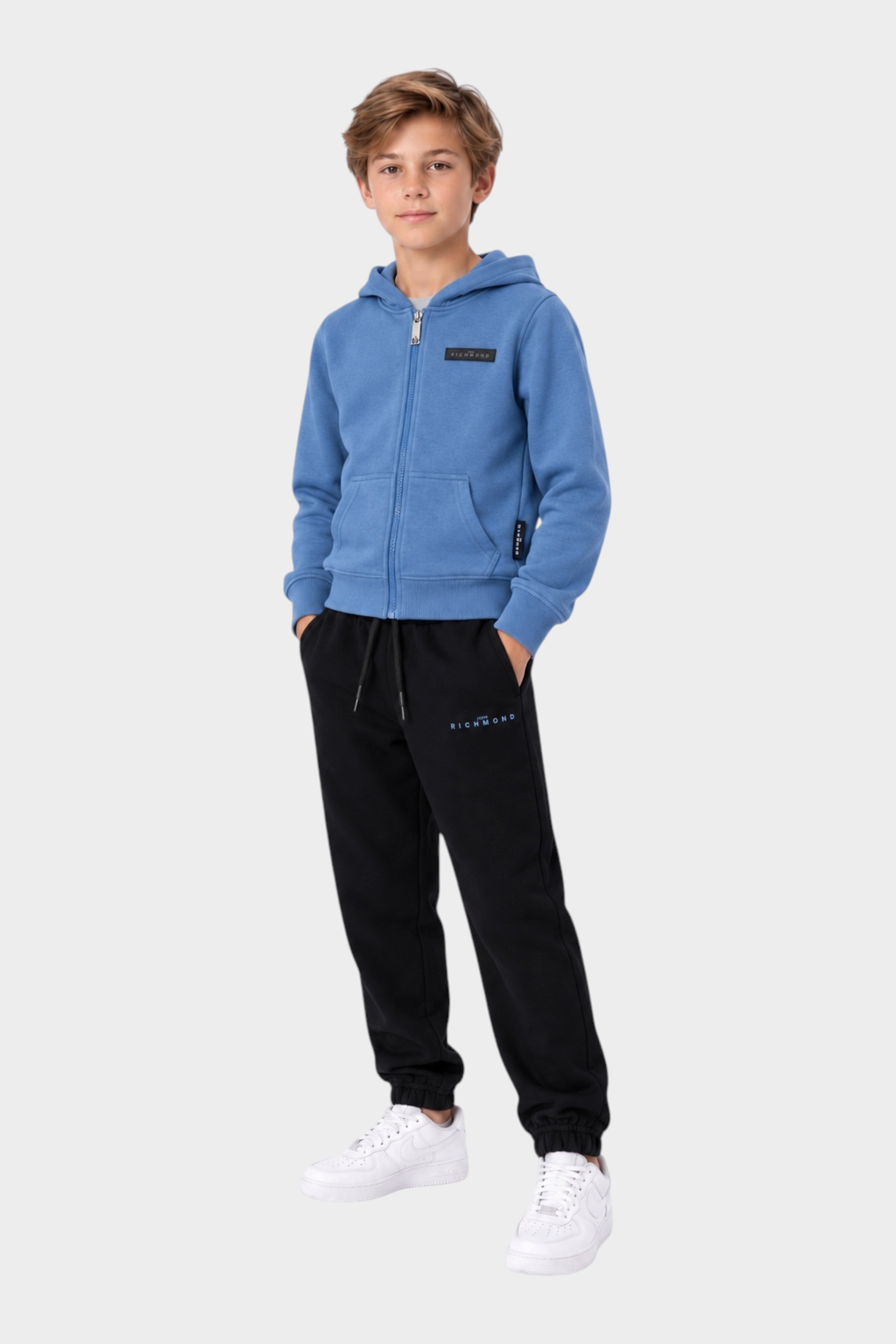 Ragazzo indossa completo sportivo Follower SRL con felpa azzurra con zip e pantaloni neri in cotone