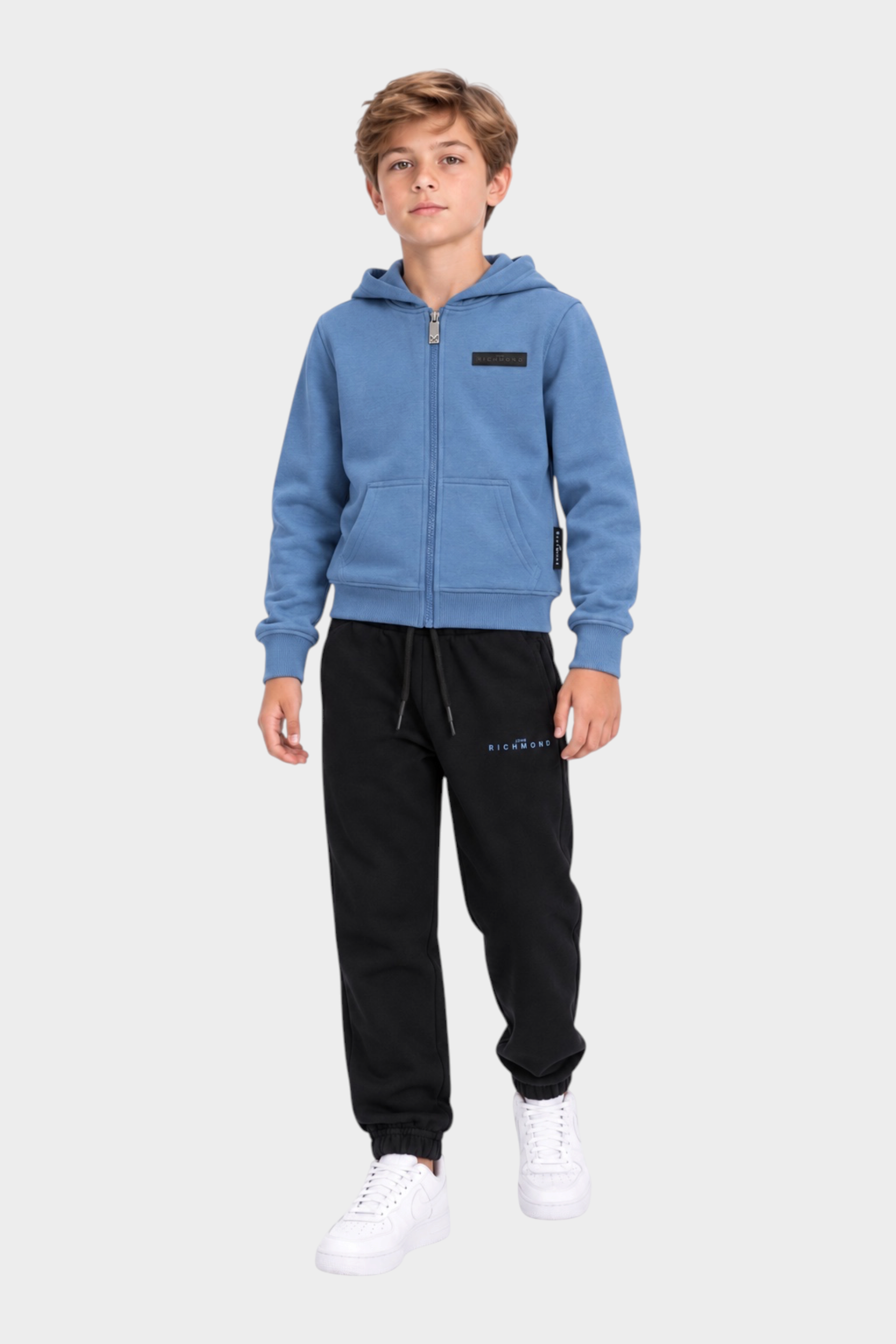 Ragazzo indossa completo sportivo Follower SRL con felpa azzurra con zip e pantaloni neri in cotone