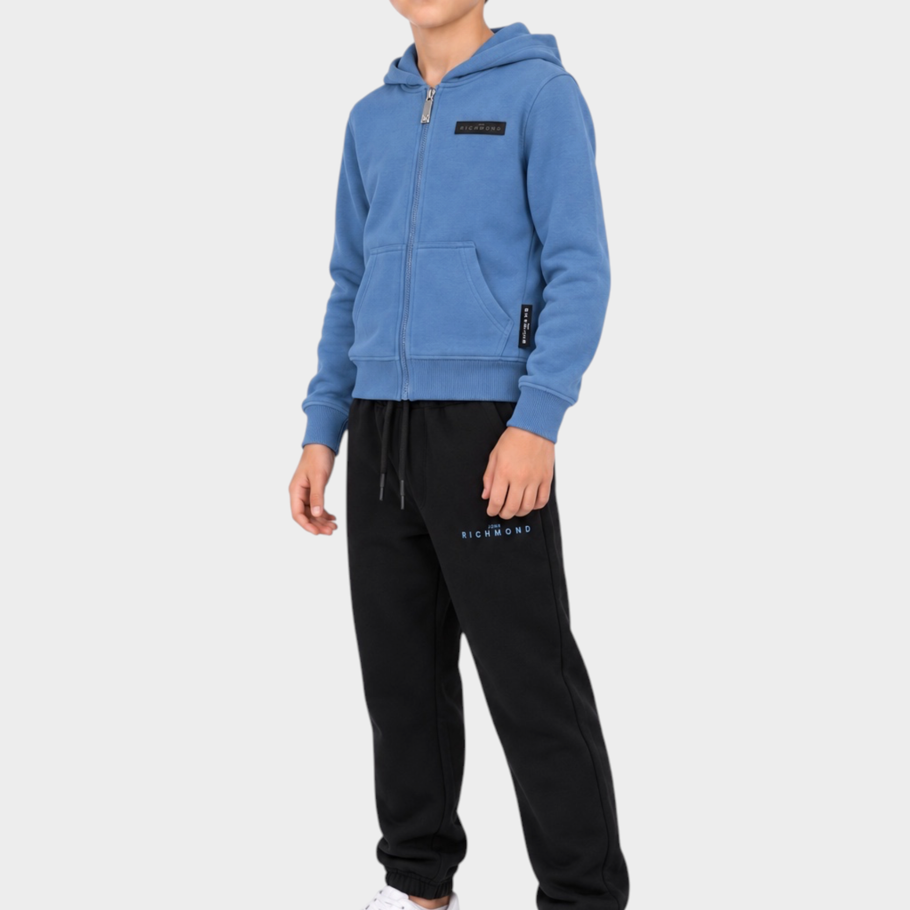 Ragazzo indossa completo sportivo Follower SRL con felpa azzurra con zip e pantaloni neri con logo RICHMOND