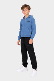 Ragazzo indossa completo sportivo Follower SRL con felpa azzurra con zip e pantaloni neri con logo RICHMOND