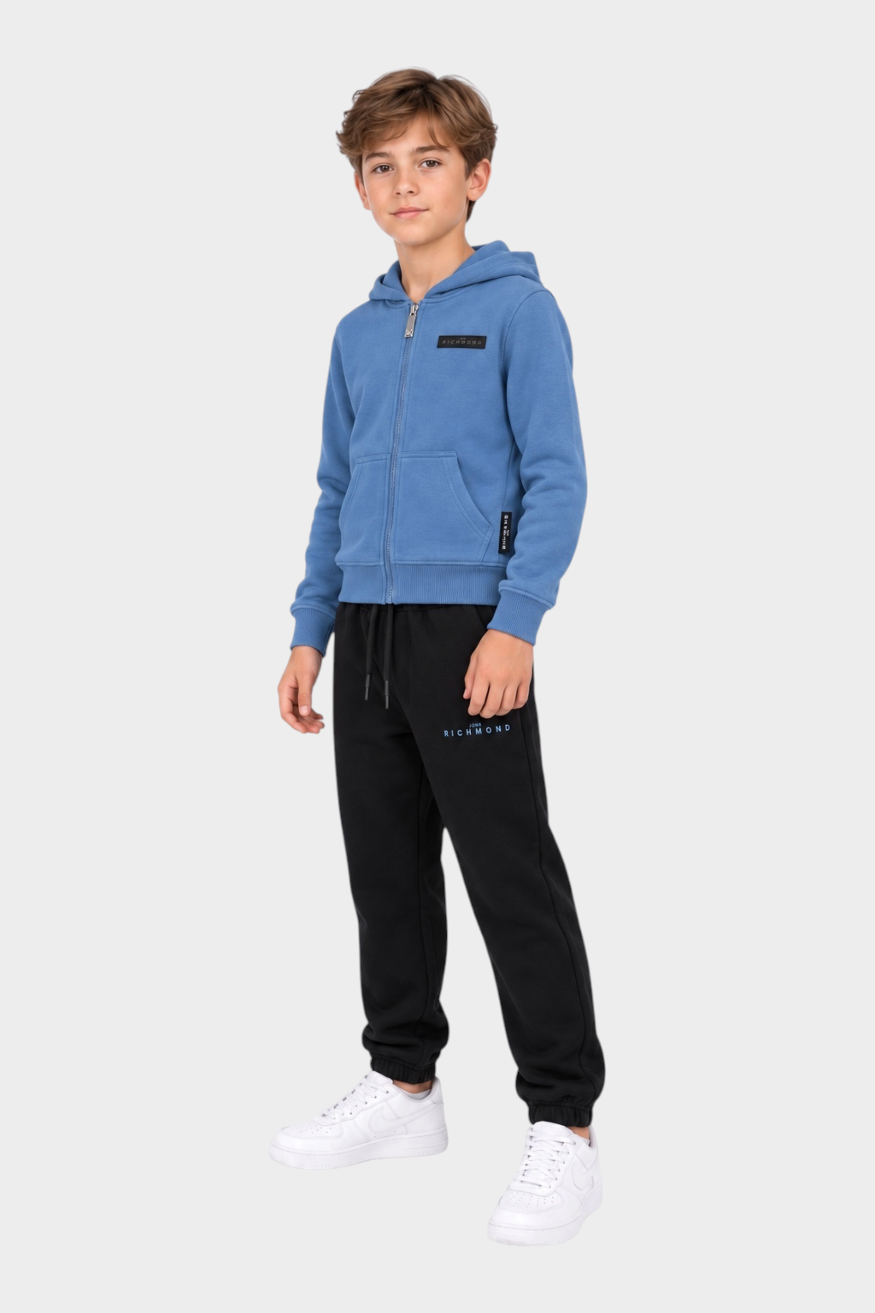 Ragazzo indossa completo sportivo Follower SRL con felpa azzurra con zip e pantaloni neri con logo RICHMOND