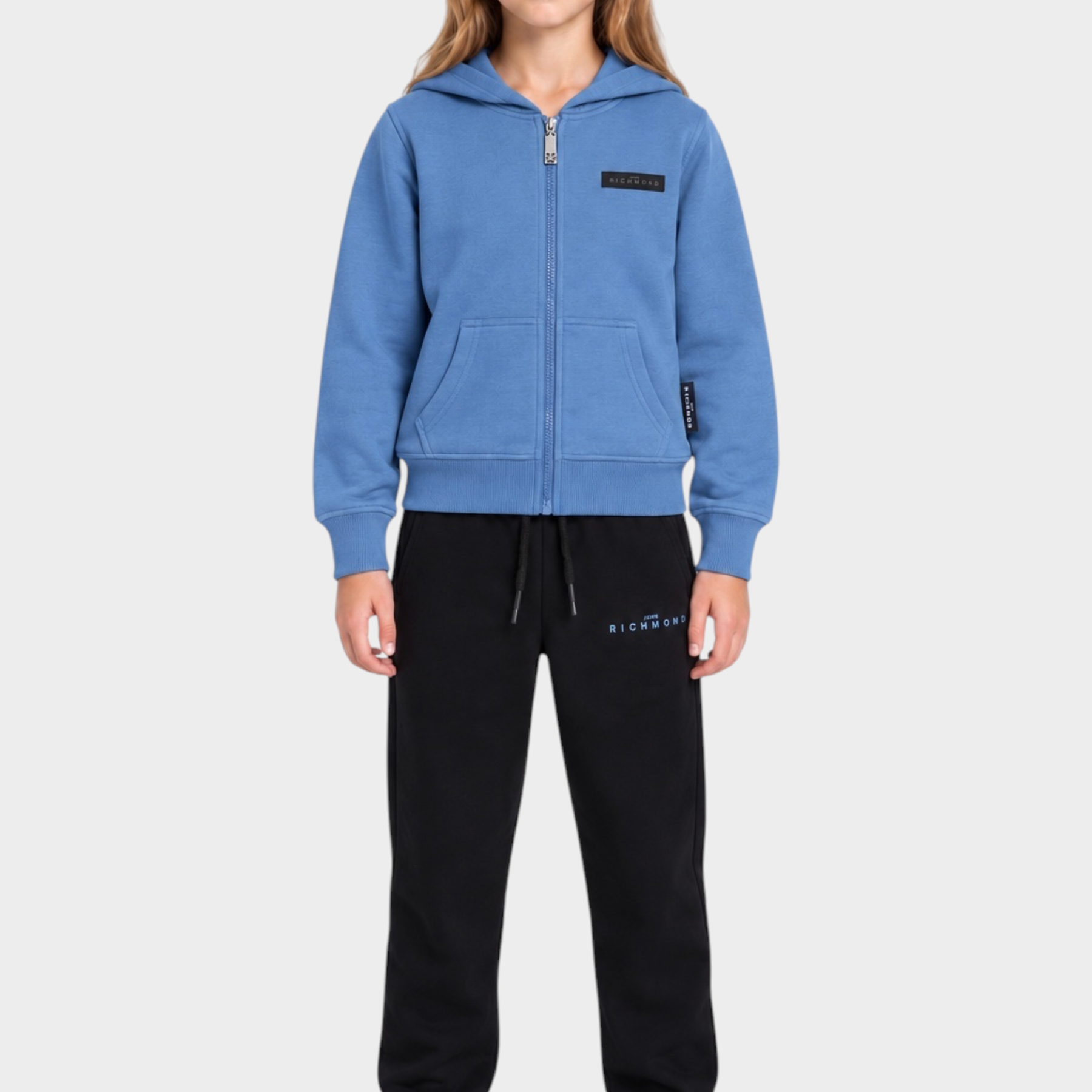 Ragazza indossa completo sportivo Follower SRL con felpa azzurra con zip e pantaloni neri in cotone