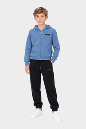 Ragazzo indossa completo sportivo Follower SRL con felpa azzurra con zip e pantaloni neri con logo RICHMOND