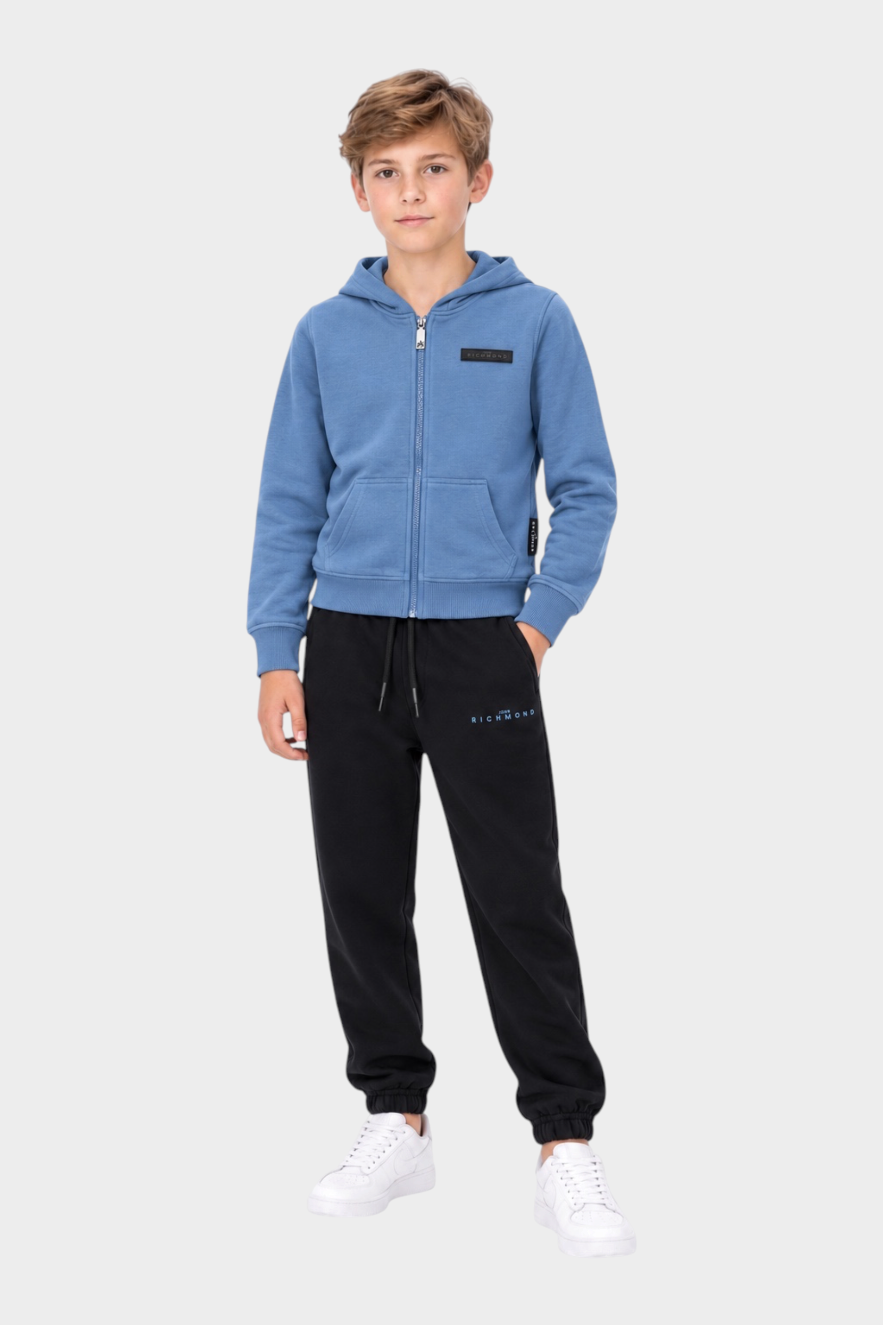 Ragazzo indossa completo sportivo Follower SRL con felpa azzurra con zip e pantaloni neri con logo RICHMOND
