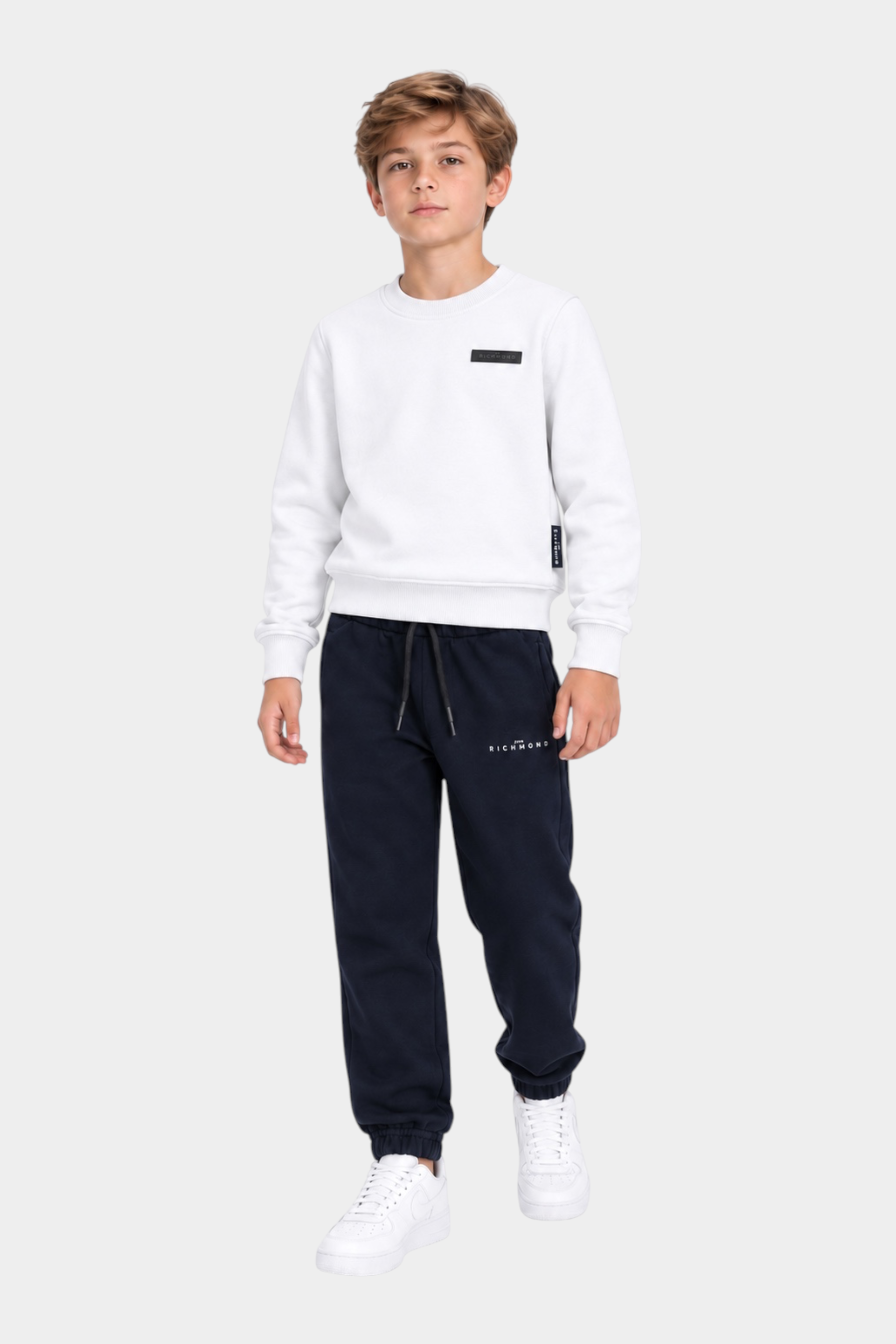 Ragazzo indossa completo sportivo Follower SRL con felpa bianca e pantaloni jogger blu scuro con logo RICHMOND