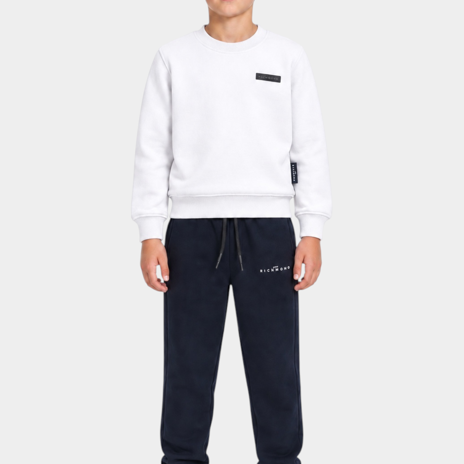 Ragazzo indossa completo sportivo Follower SRL con felpa bianca e pantaloni della tuta blu scuro con logo RICHMOND