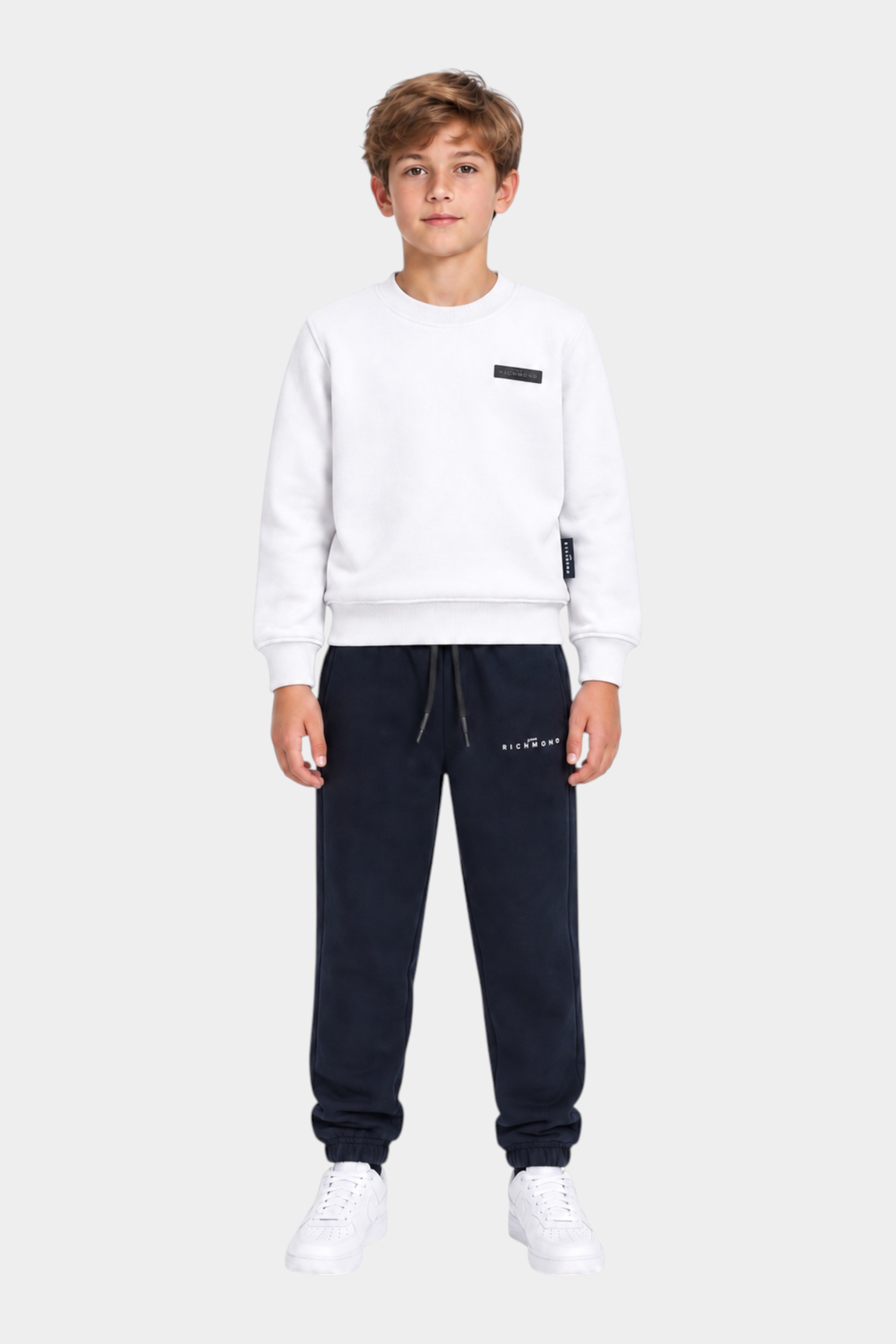 Ragazzo indossa completo sportivo Follower SRL con felpa bianca e pantaloni della tuta blu scuro con logo RICHMOND