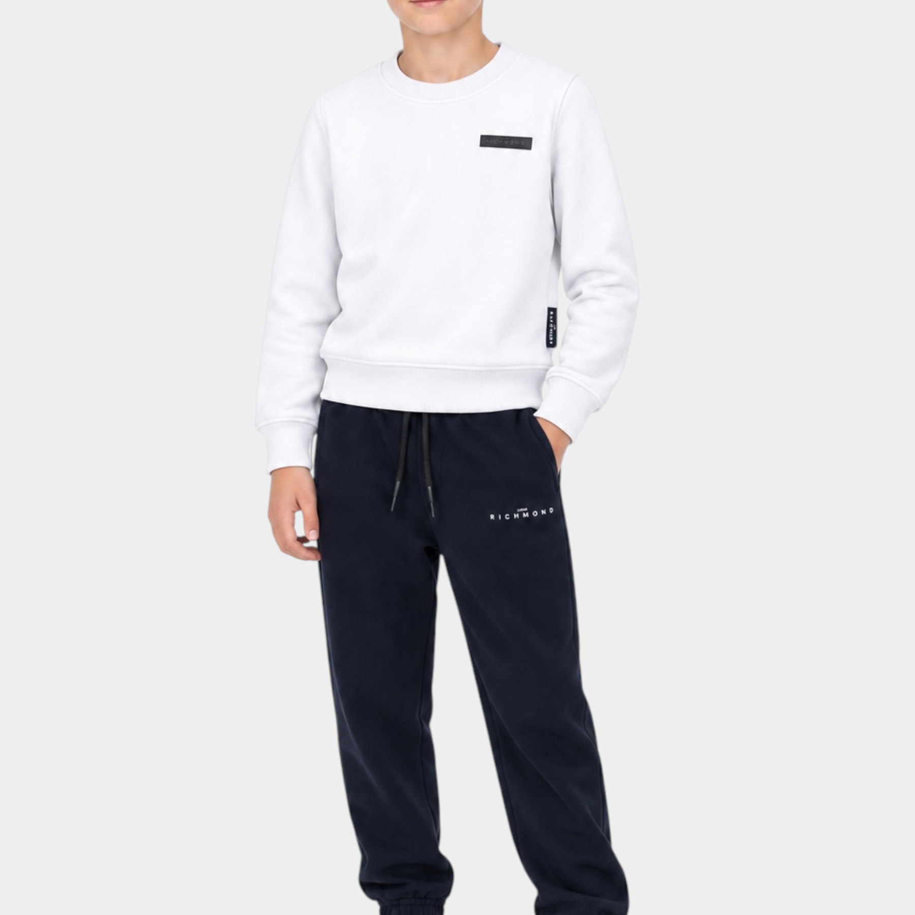 Ragazzo indossa completo sportivo Follower SRL con felpa bianca e pantaloni neri con logo RICHMOND