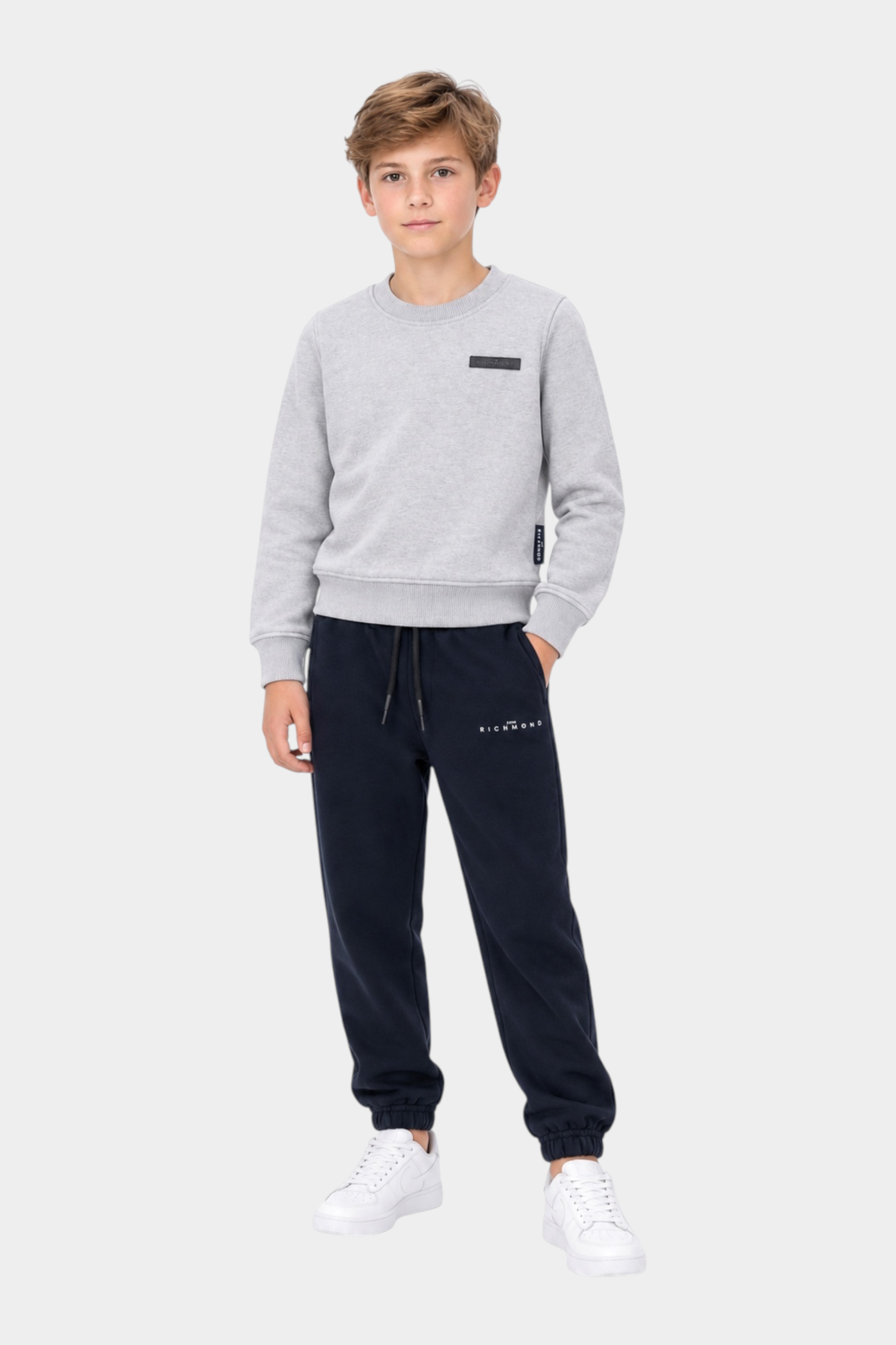 Ragazzo indossa un completo sportivo Follower SRL con felpa grigia a girocollo e pantaloni della tuta blu navy