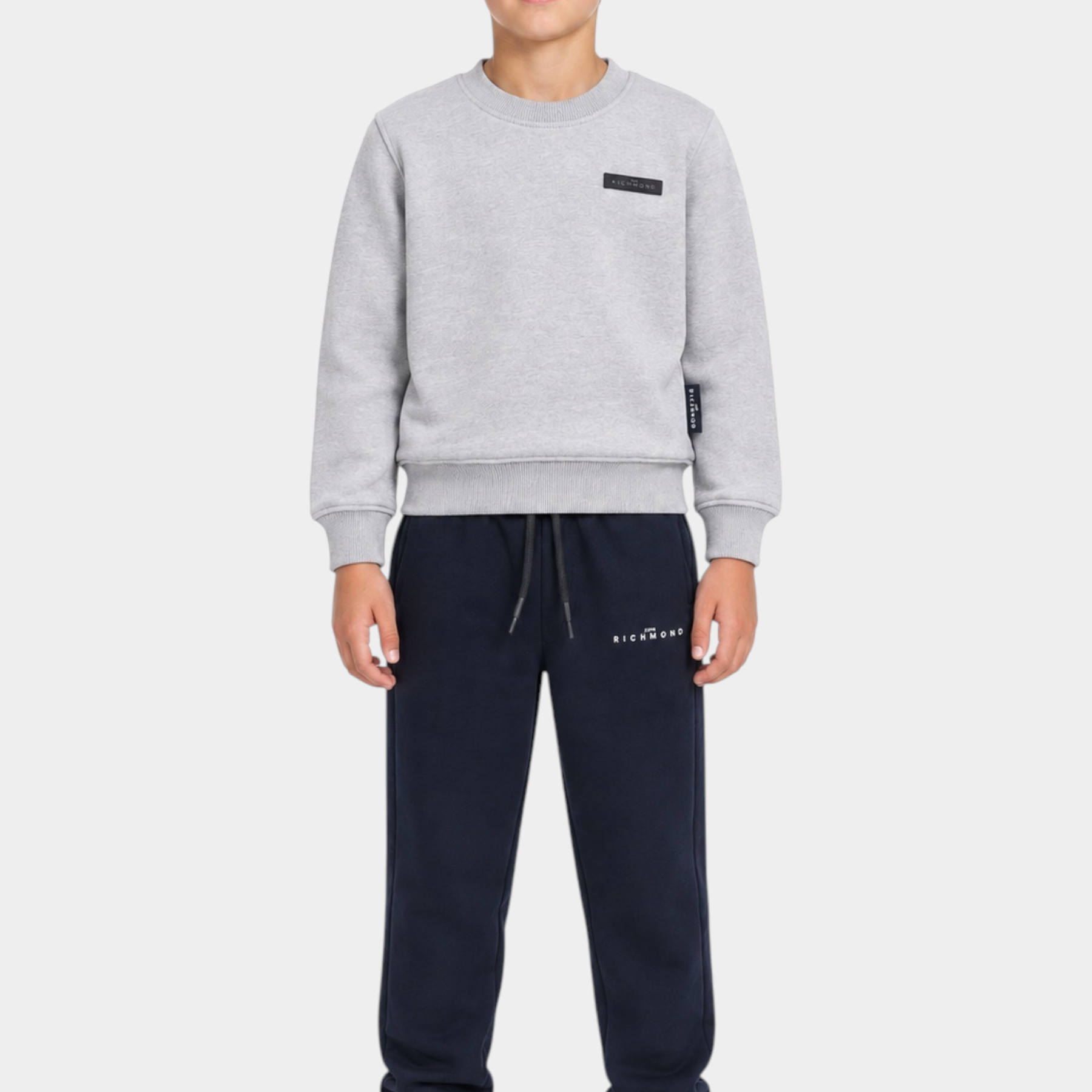 Ragazzo indossa completo sportivo Follower SRL con felpa grigia e pantaloni jogger blu navy con logo RICHMOND