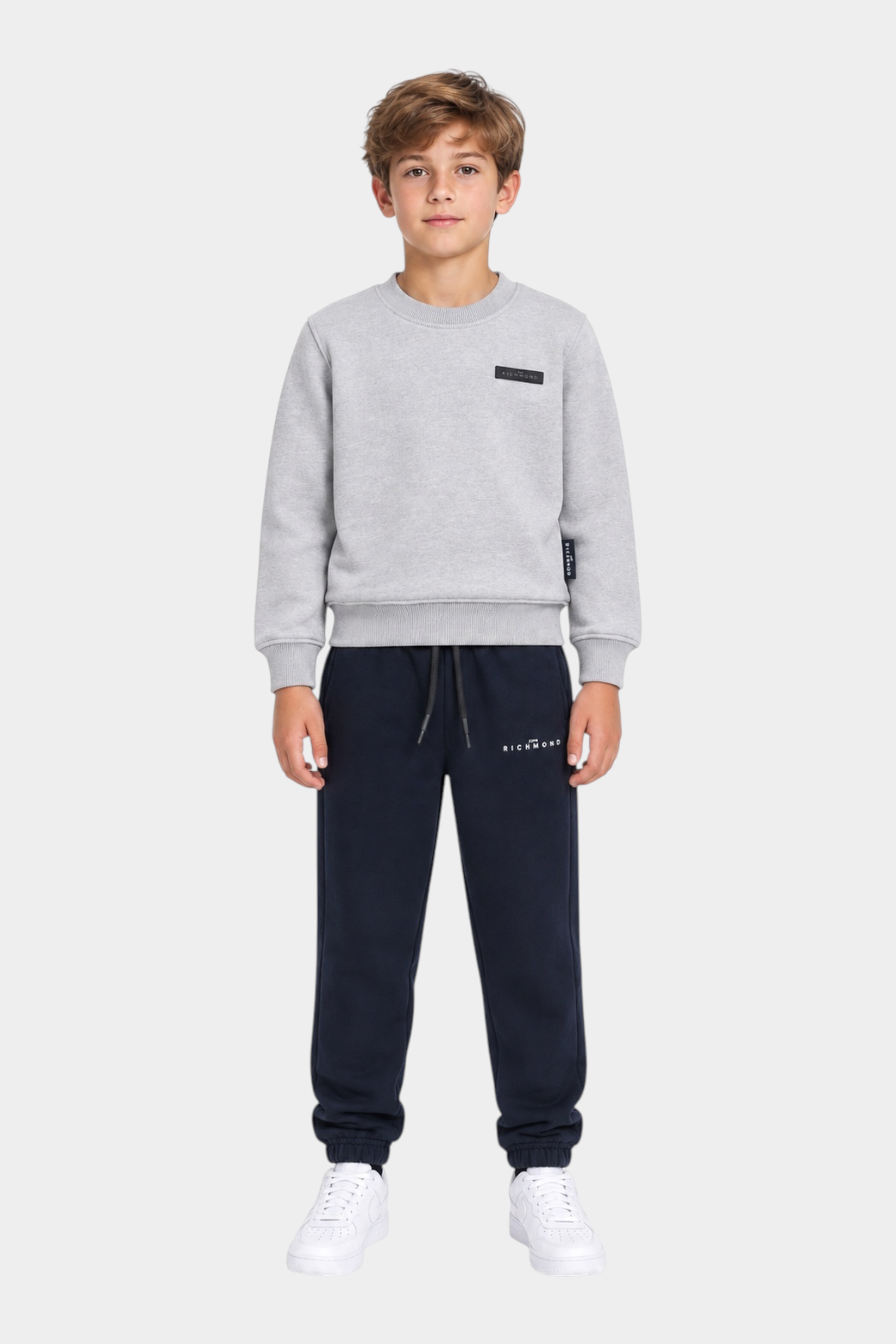 Ragazzo indossa completo sportivo Follower SRL con felpa grigia e pantaloni jogger blu navy con logo RICHMOND