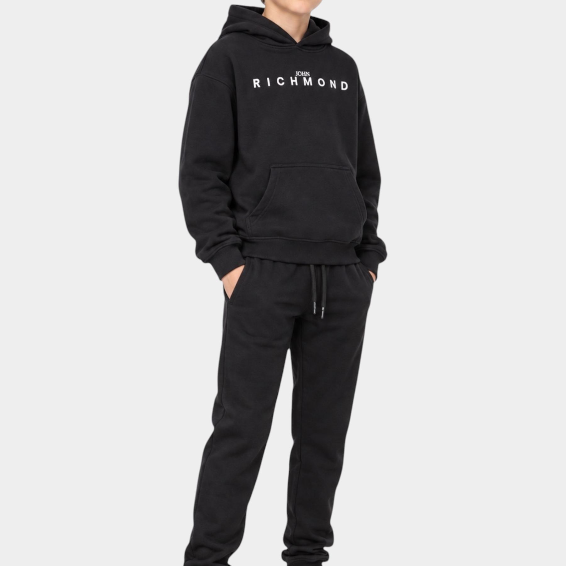 Ragazzo indossa un completo sportivo nero Follower SRL con felpa con cappuccio e logo RICHMOND e pantaloni jogger