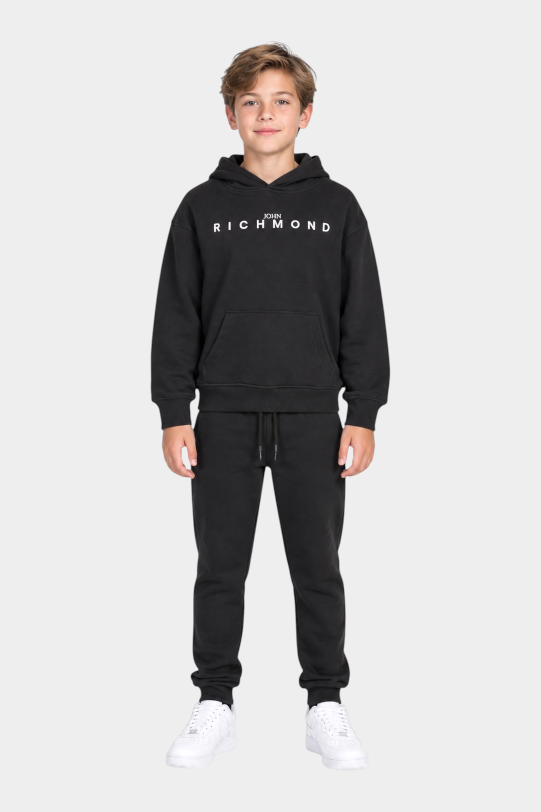 Ragazzo indossa un completo sportivo nero Follower SRL con felpa con cappuccio e logo John Richmond bianco