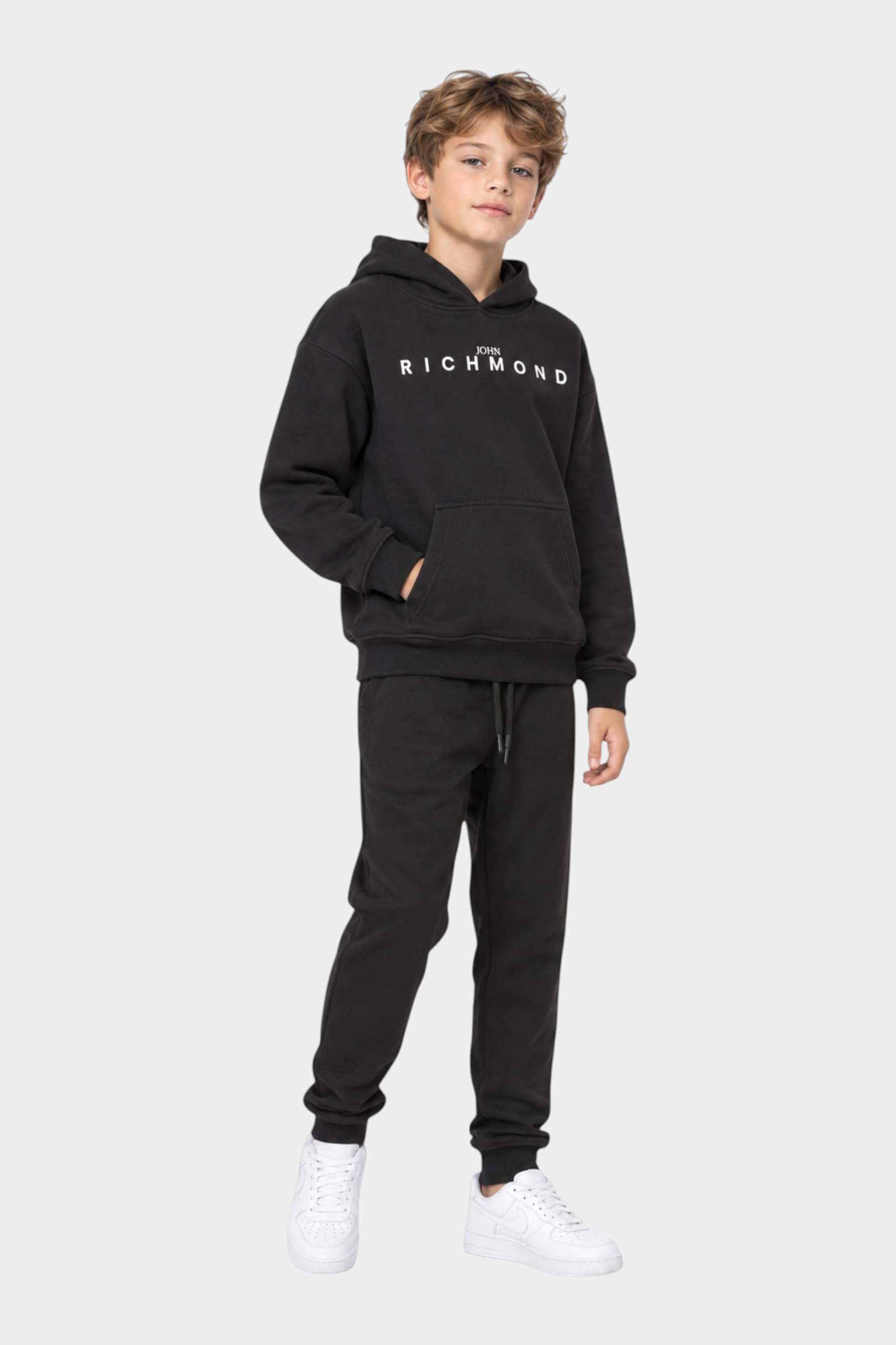 Ragazzo indossa un completo sportivo nero Follower SRL con felpa con cappuccio e logo Richmond e pantaloni jogger