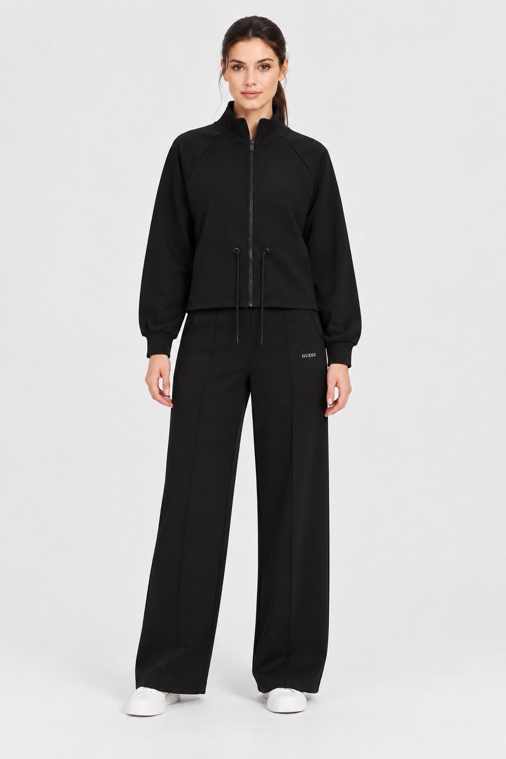Modella indossa felpa full zip nera Follower SRL con pantaloni abbinati e scarpe bianche su sfondo neutro