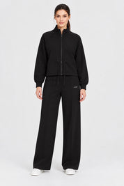 Modella indossa felpa full zip nera Follower SRL con pantaloni abbinati e scarpe bianche su sfondo neutro