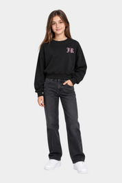 Ragazza indossa felpa girocollo nera Follower SRL con logo rosa, abbinata a jeans scuri e scarpe bianche