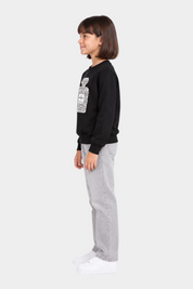 Bambina indossa felpa nera Follower SRL con stampa gioiello frontale, jeans grigi e sneakers bianche, vista laterale