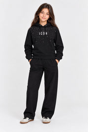 Ragazza indossa felpa nera Follower SRL con cappuccio, scritta ICON e decorazioni di strass, abbinata a pantaloni