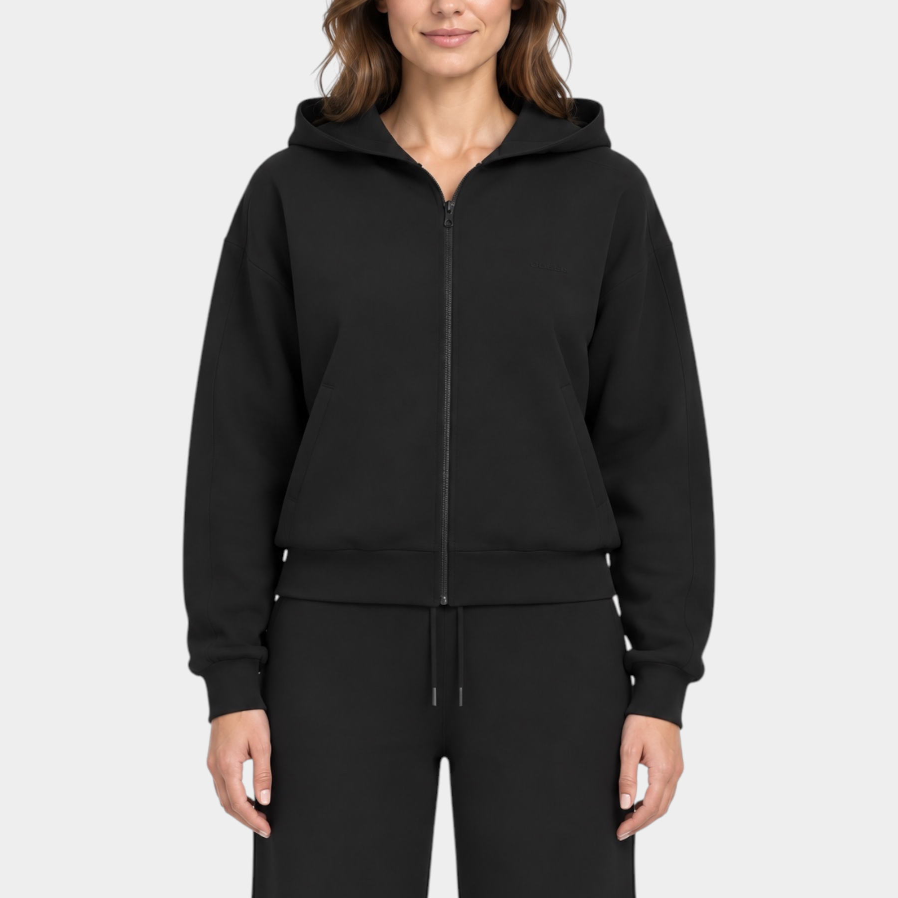 Modella indossa una felpa con cappuccio e zip intera nera GUESS, dal design minimalista e vestibilità confortevole.
