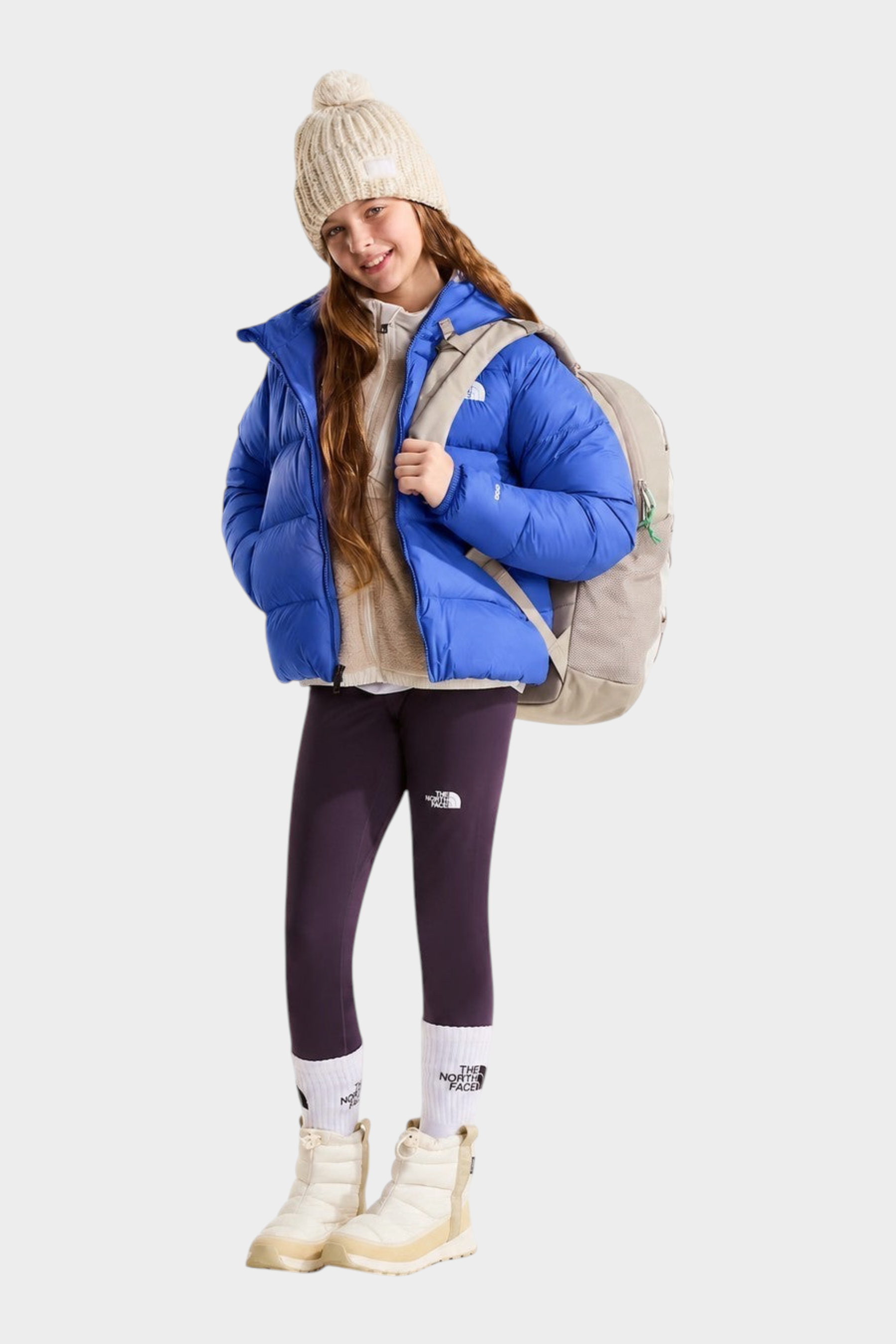 Ragazza indossa giacca in piumino blu con cappuccio THE NORTH FACE di Follower SRL con zaino e leggings viola