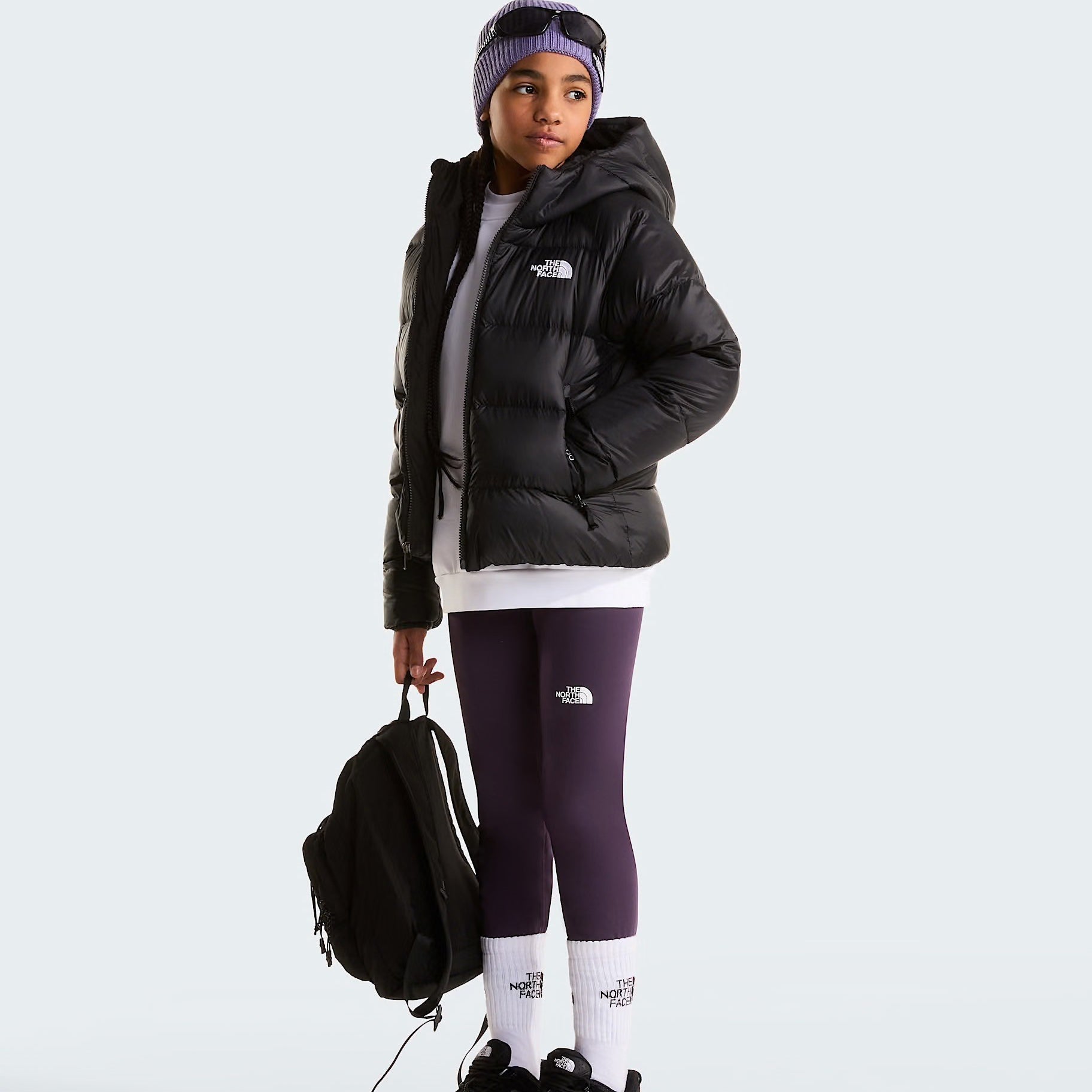Modella indossa giacca in piumino nera con cappuccio Follower SRL Hydrenalite, leggings viola e zaino nero.