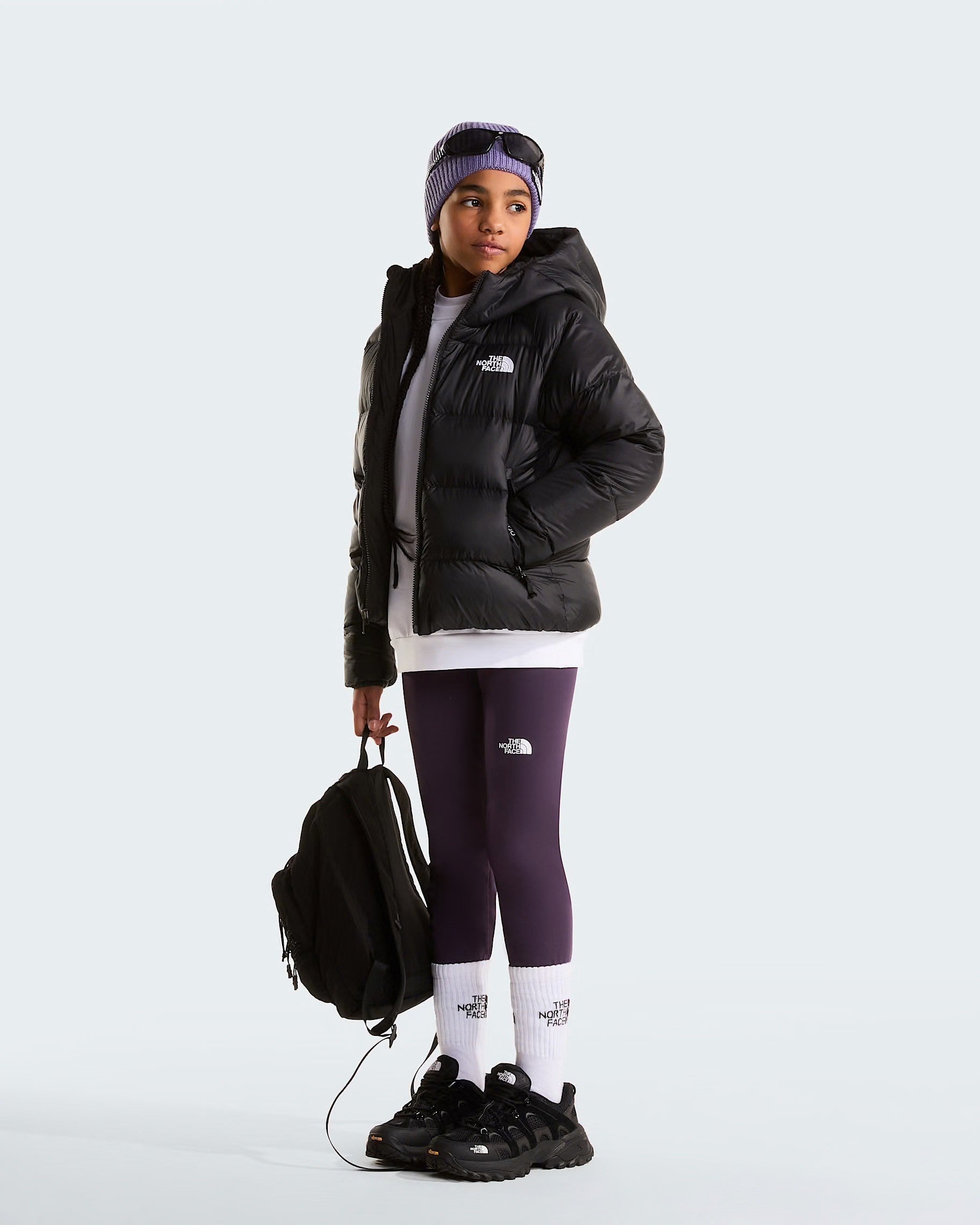 Modella indossa giacca in piumino nera con cappuccio Follower SRL Hydrenalite, leggings viola e zaino nero.