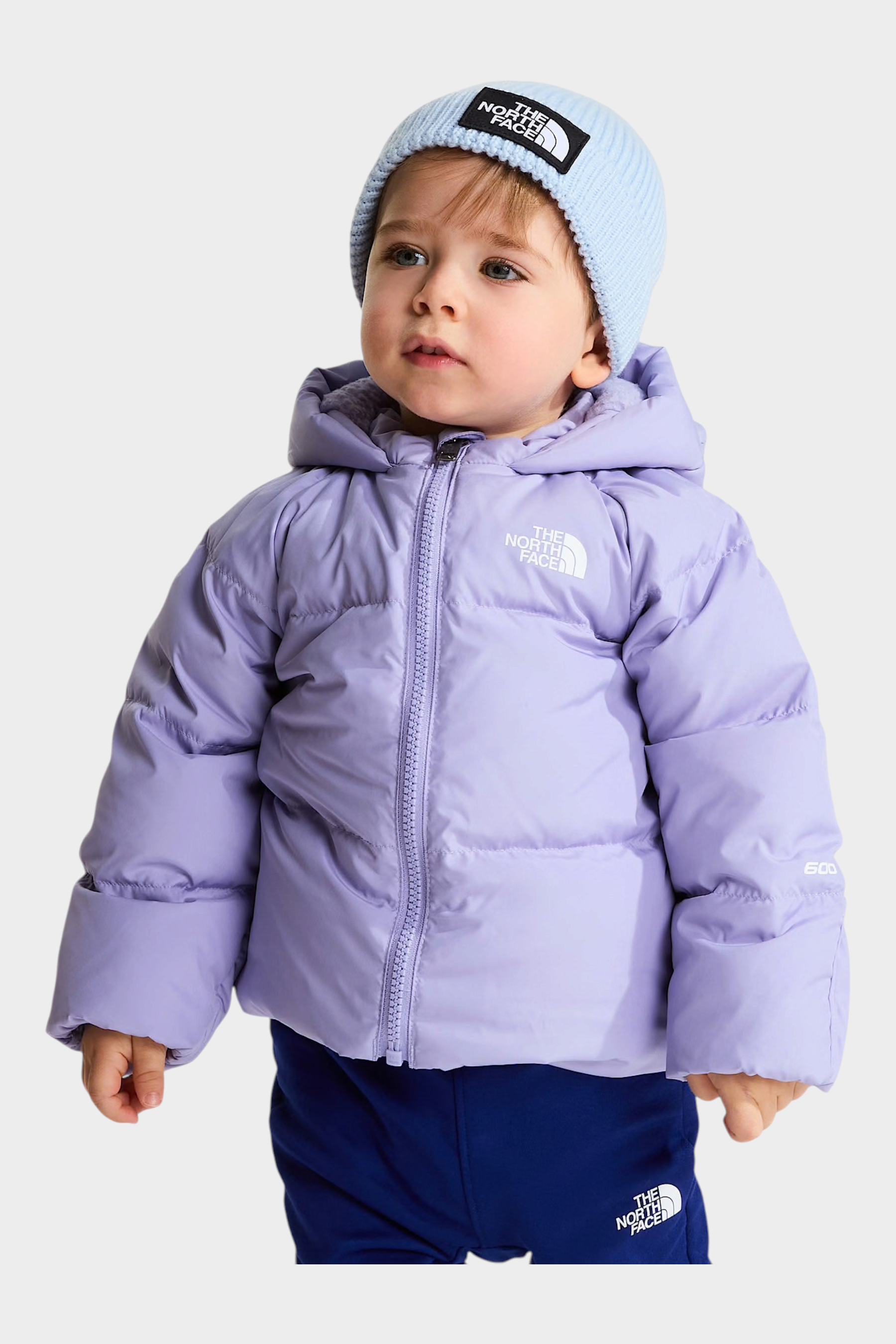 Bambino che indossa una giacca in piumino viola Follower SRL con cappuccio e berretto azzurro The North Face