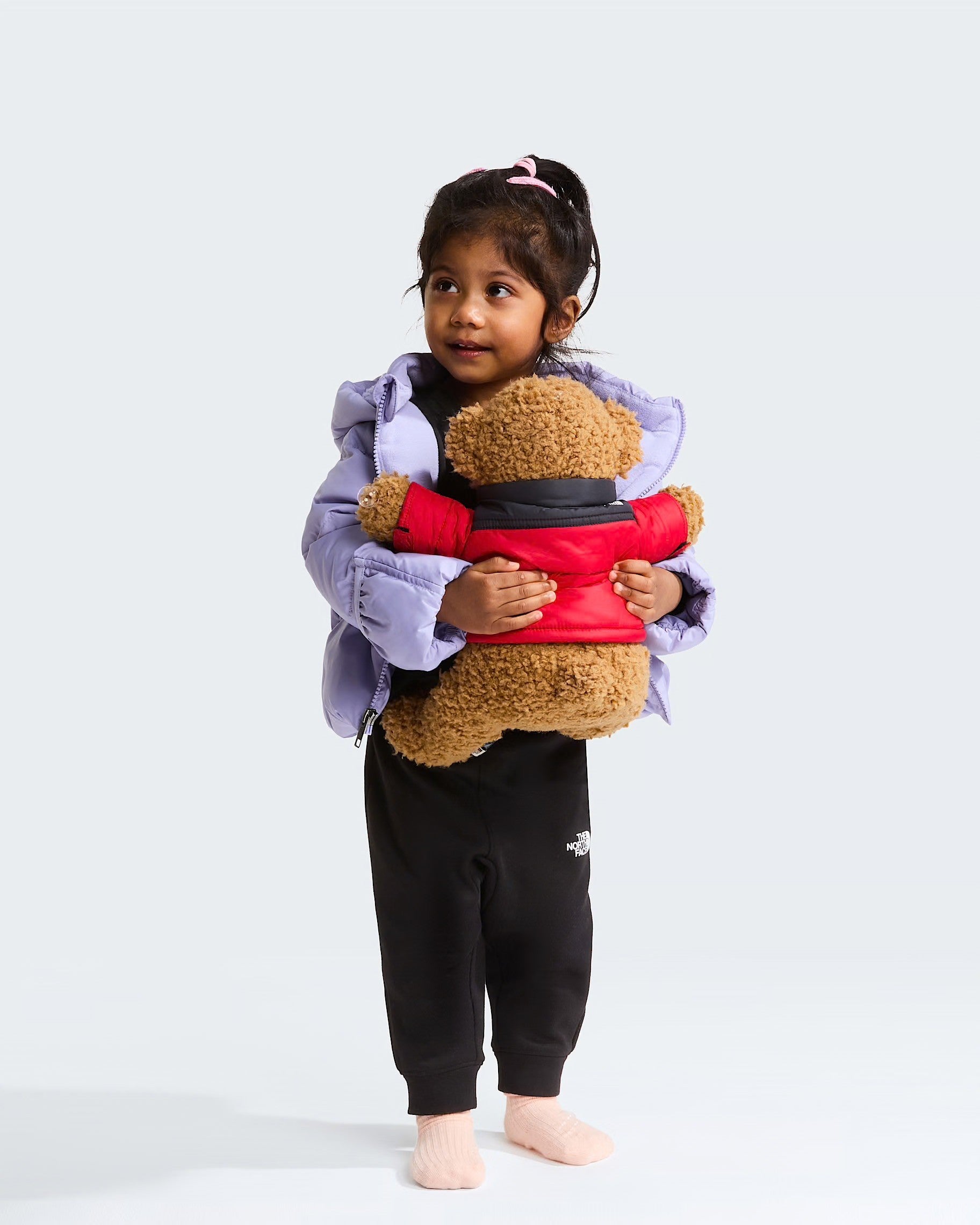 Bambina che indossa giacca in piumino viola Follower SRL THE NORTH FACE mentre abbraccia un orsacchiotto