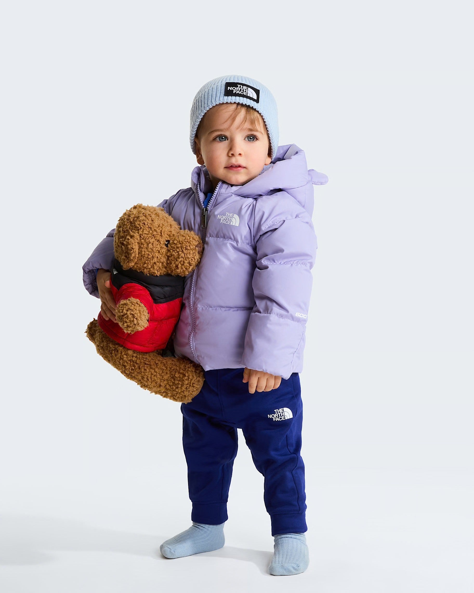 Bambino con giacca in piumino viola The North Face e berretto azzurro, proposta da Follower SRL
