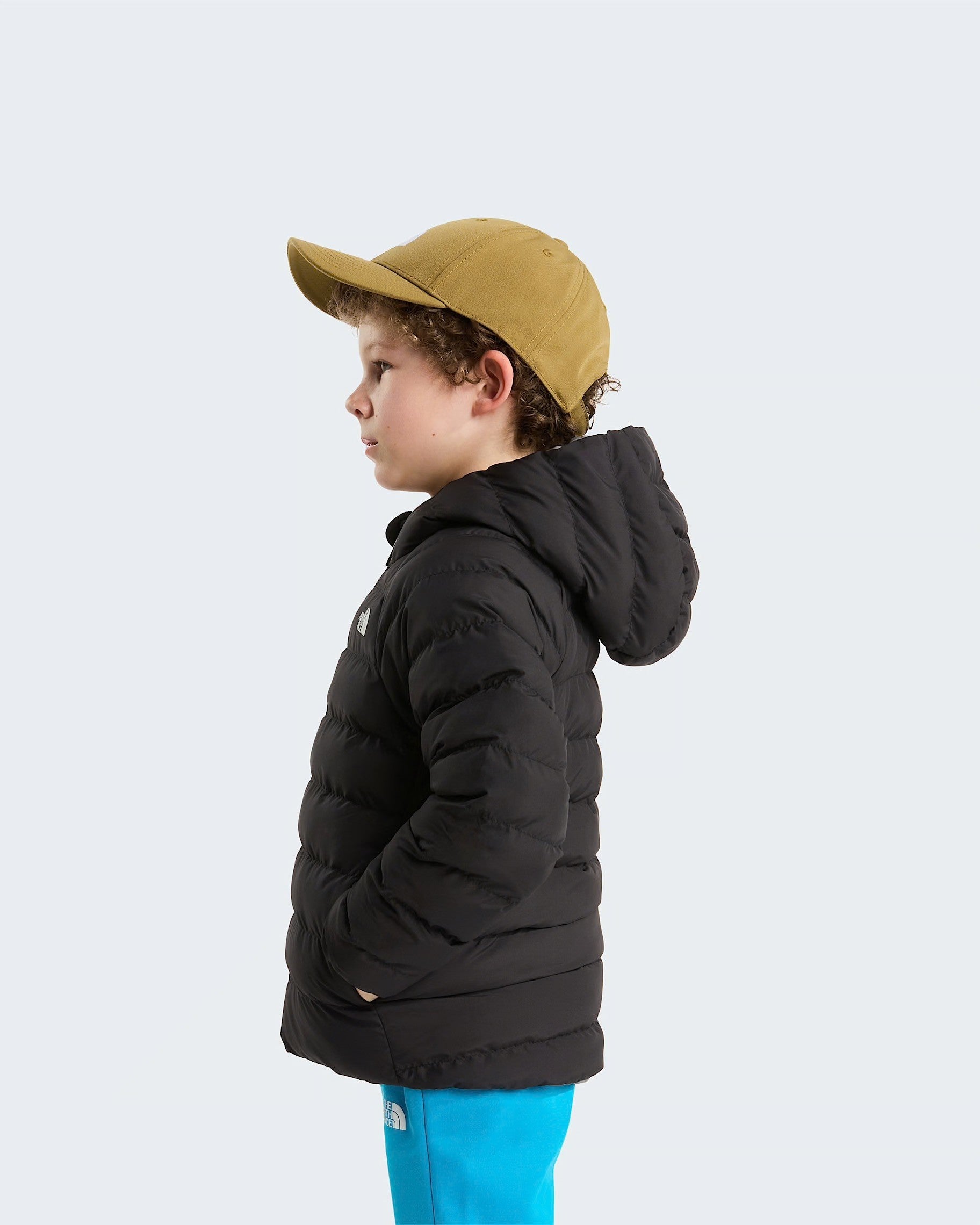 Bambino di profilo indossa giacca reversibile imbottita nera con cappuccio Follower SRL e cappellino color senape
