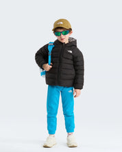 Bambino indossa giacca reversibile imbottita nera con cappuccio Follower SRL, pantaloni azzurri e cappellino beige