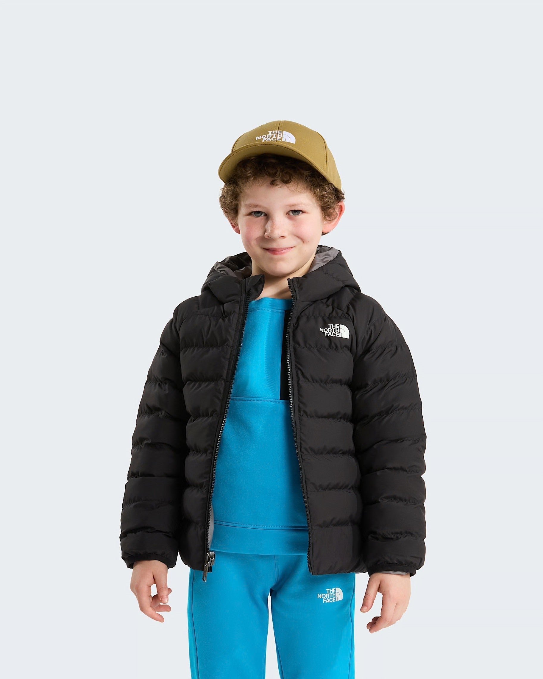 Bambino che indossa una giacca reversibile imbottita nera con cappuccio Follower SRL e cappellino color oliva